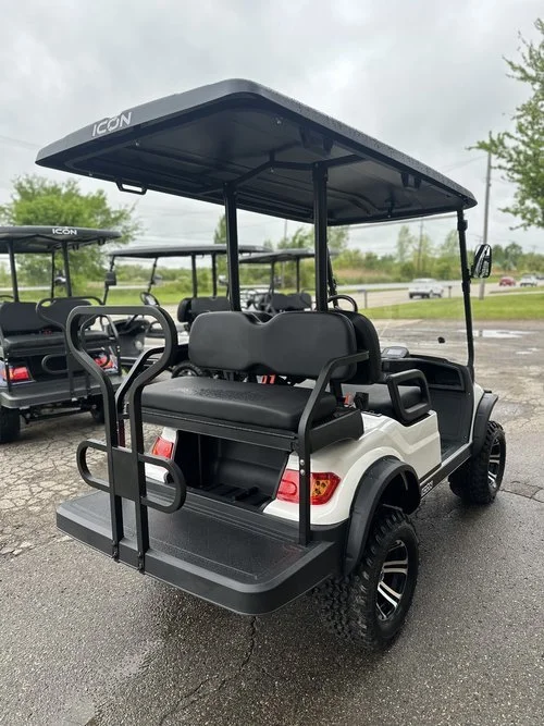 White golf cart with black roof and seating, parked outdoors on a paved lot, with other golf carts visible in background.