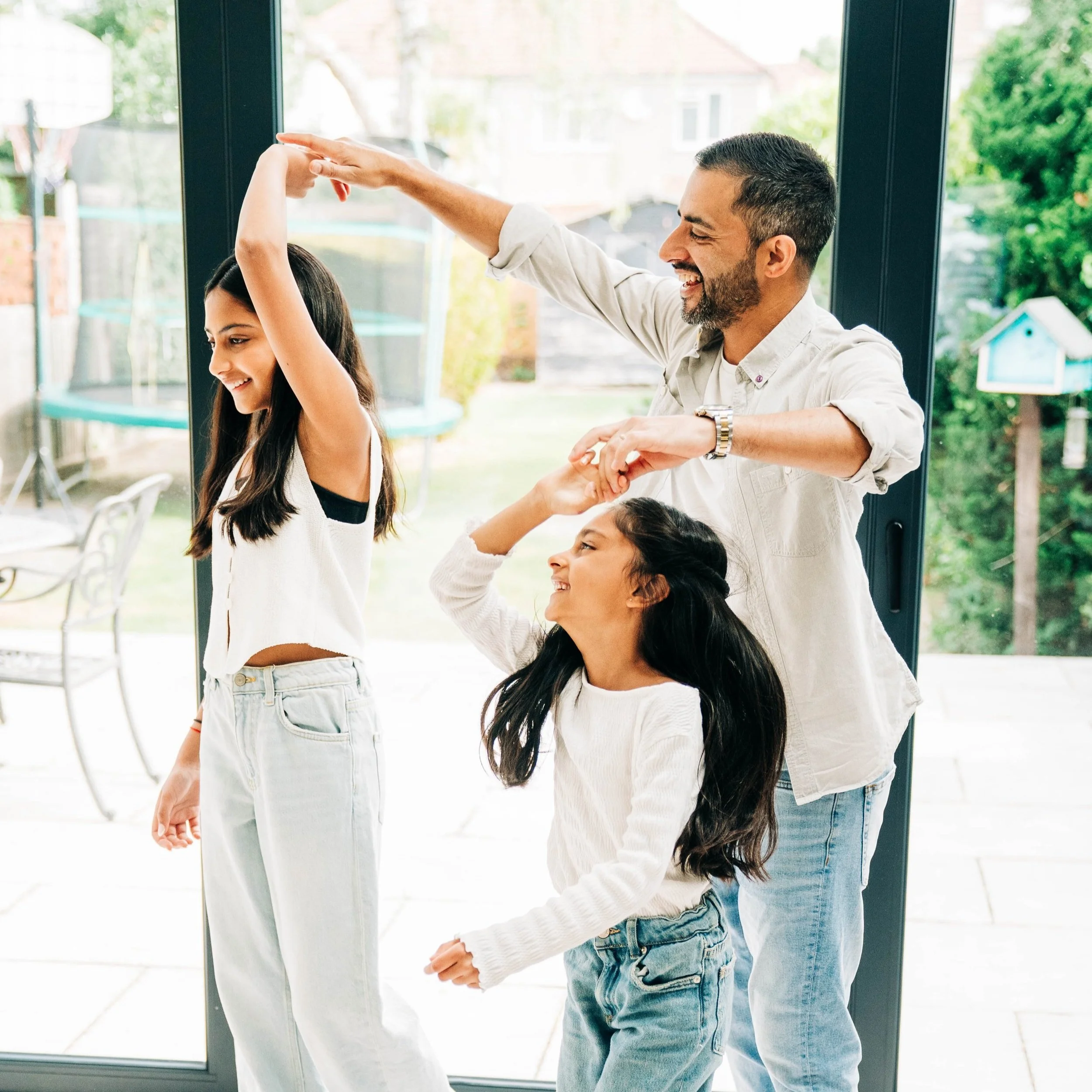 A family of three dancing happily inside their home.
