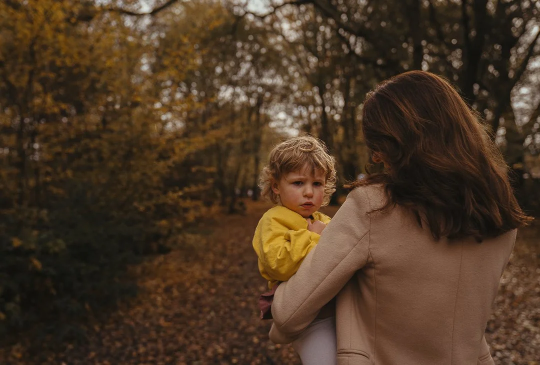 A woman holding a young girl in an autumnal forest.