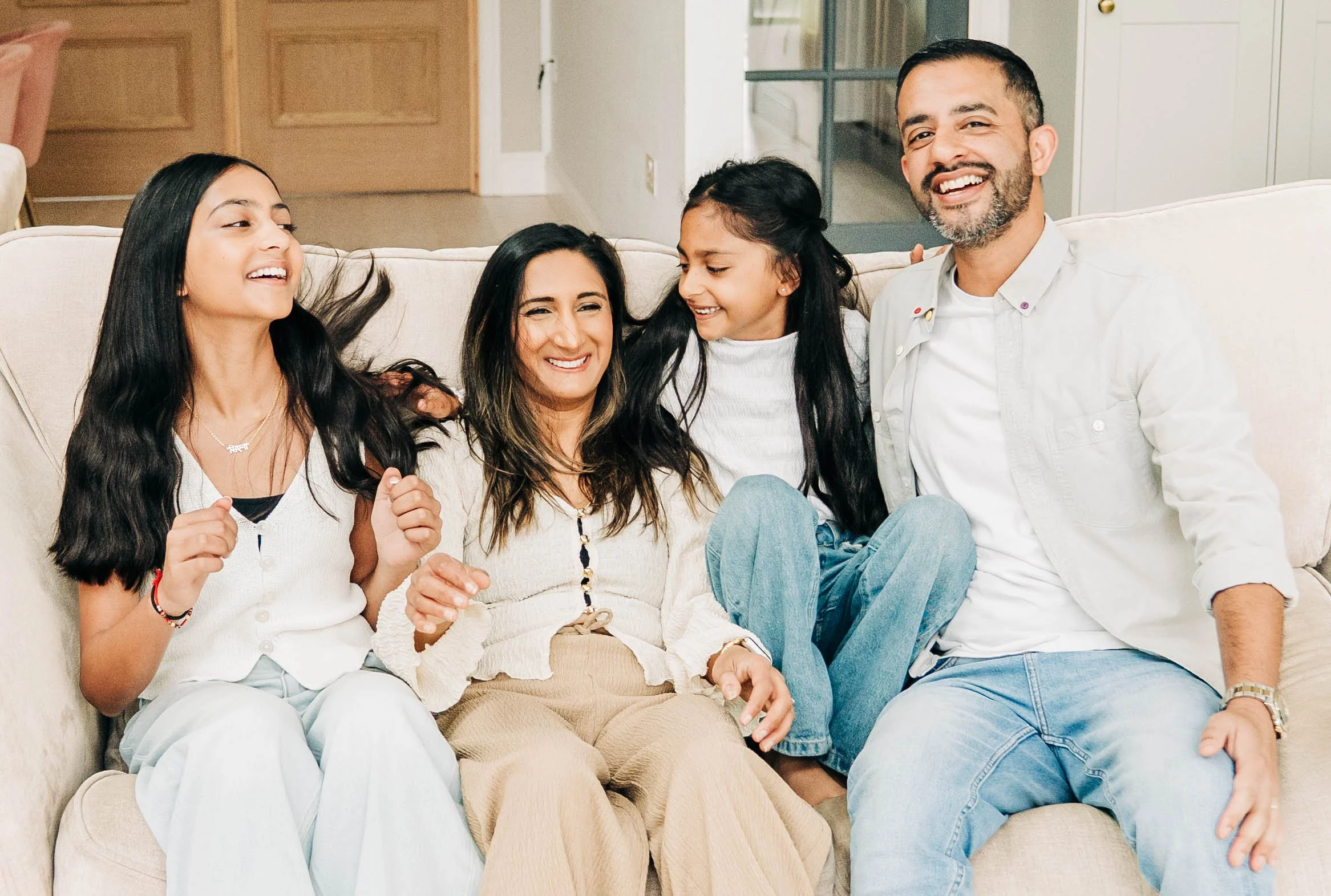 A family of five sitting on a beige couch, smiling and enjoying each other's company in a living room.