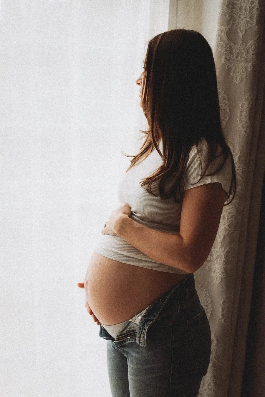A pregnant women looking out of the window cradling her belly 