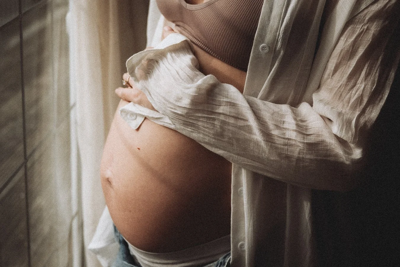 A pregnant women looking out of the window cradling her belly- light from the window reflecting on the bump