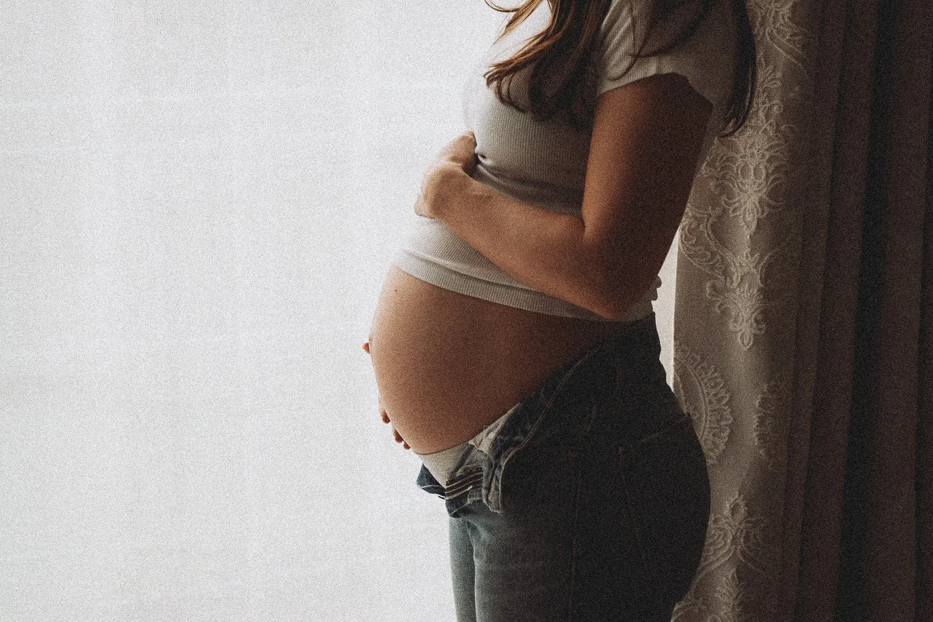 A pregnant women looking out of the window cradling her belly 