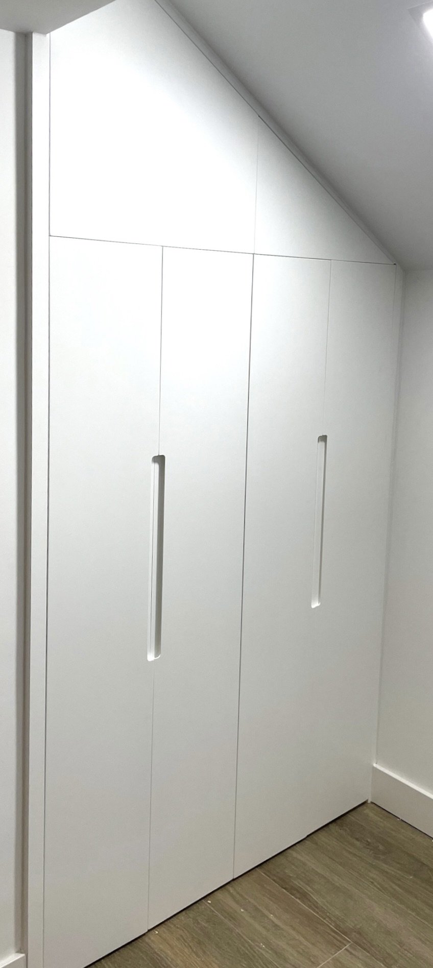 Armario a medida abuhardillado de puertas abatibles con uñero rectangular central lacado en blanco