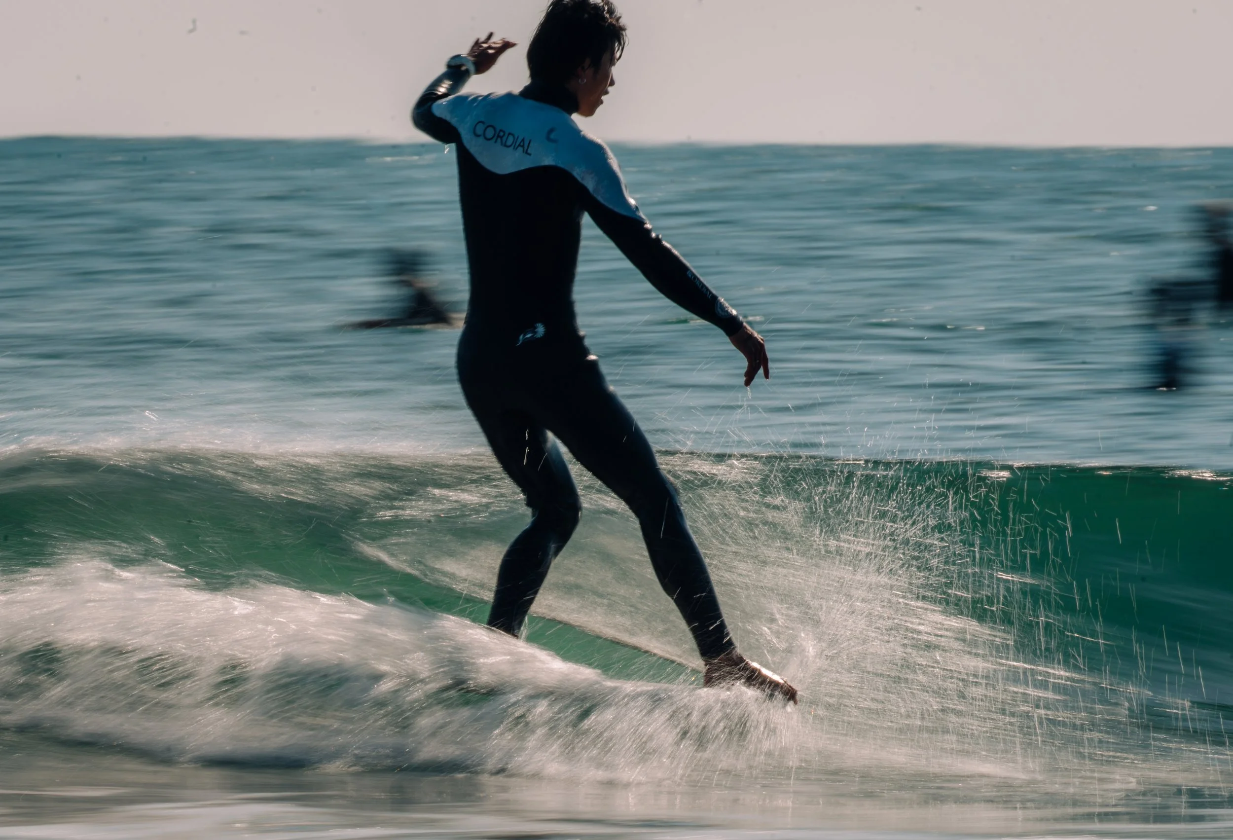 Person wearing a wetsuit riding a surfboard on a wave at the beach during sunset