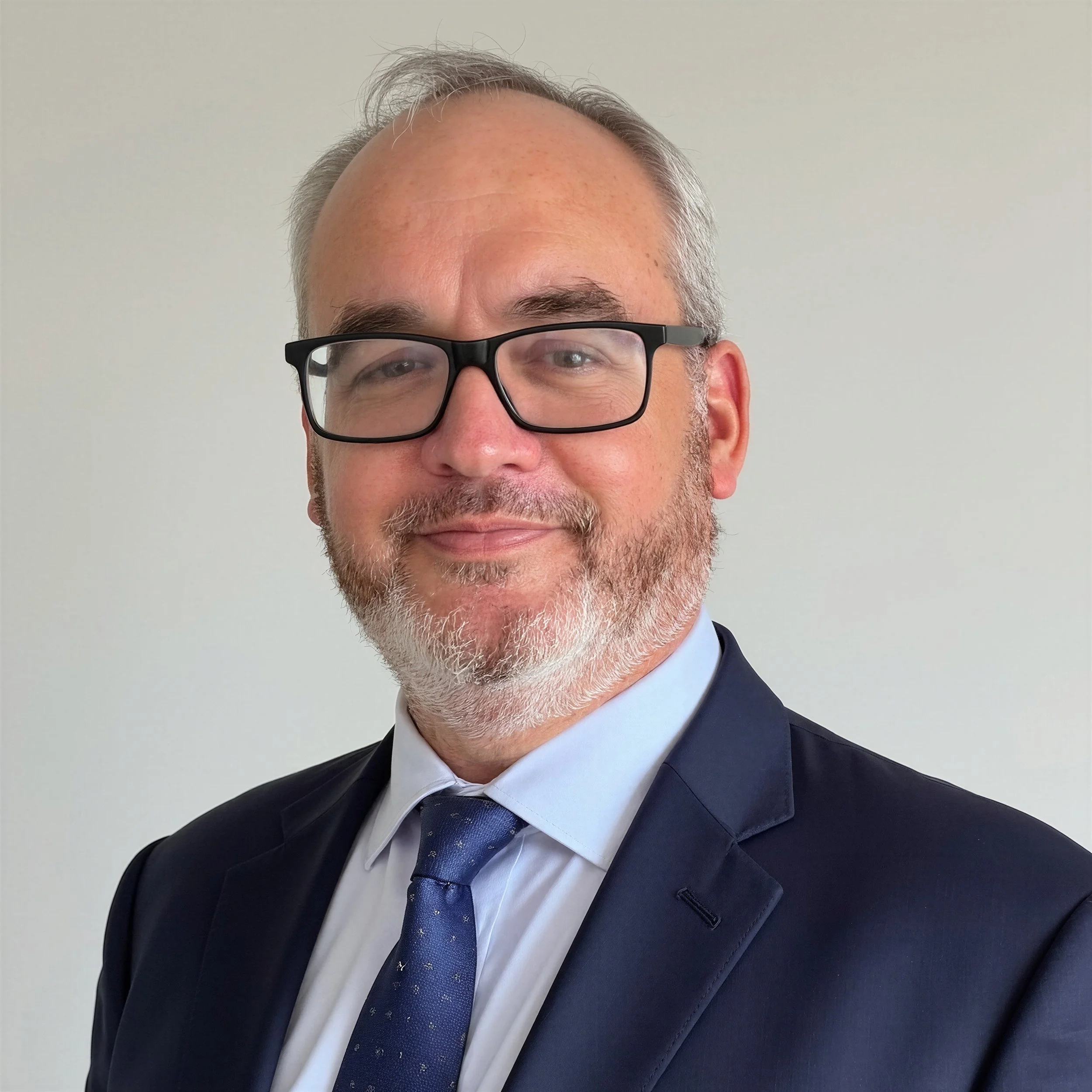 Man in a suit with glasses and an orange tie smiling indoors