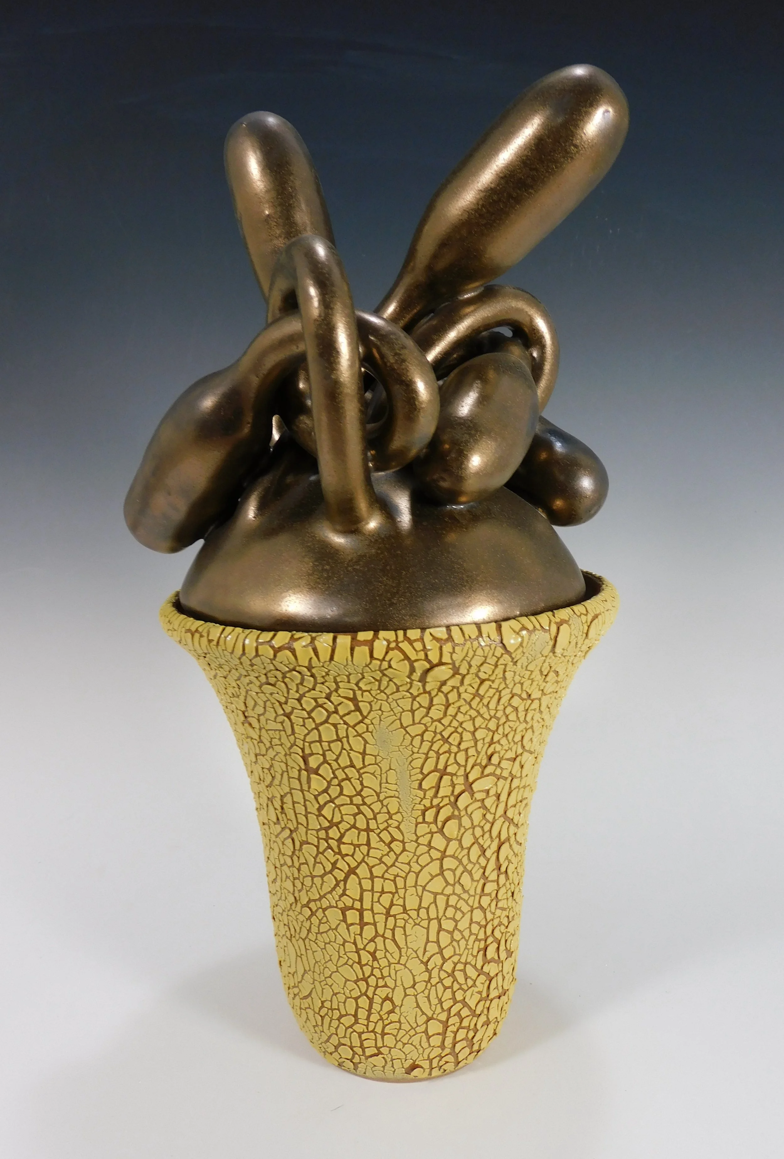 A sculpture of a bunch of abstract, elongated shapes in a dark metallic finish, placed in a yellow, textured ceramic pot.