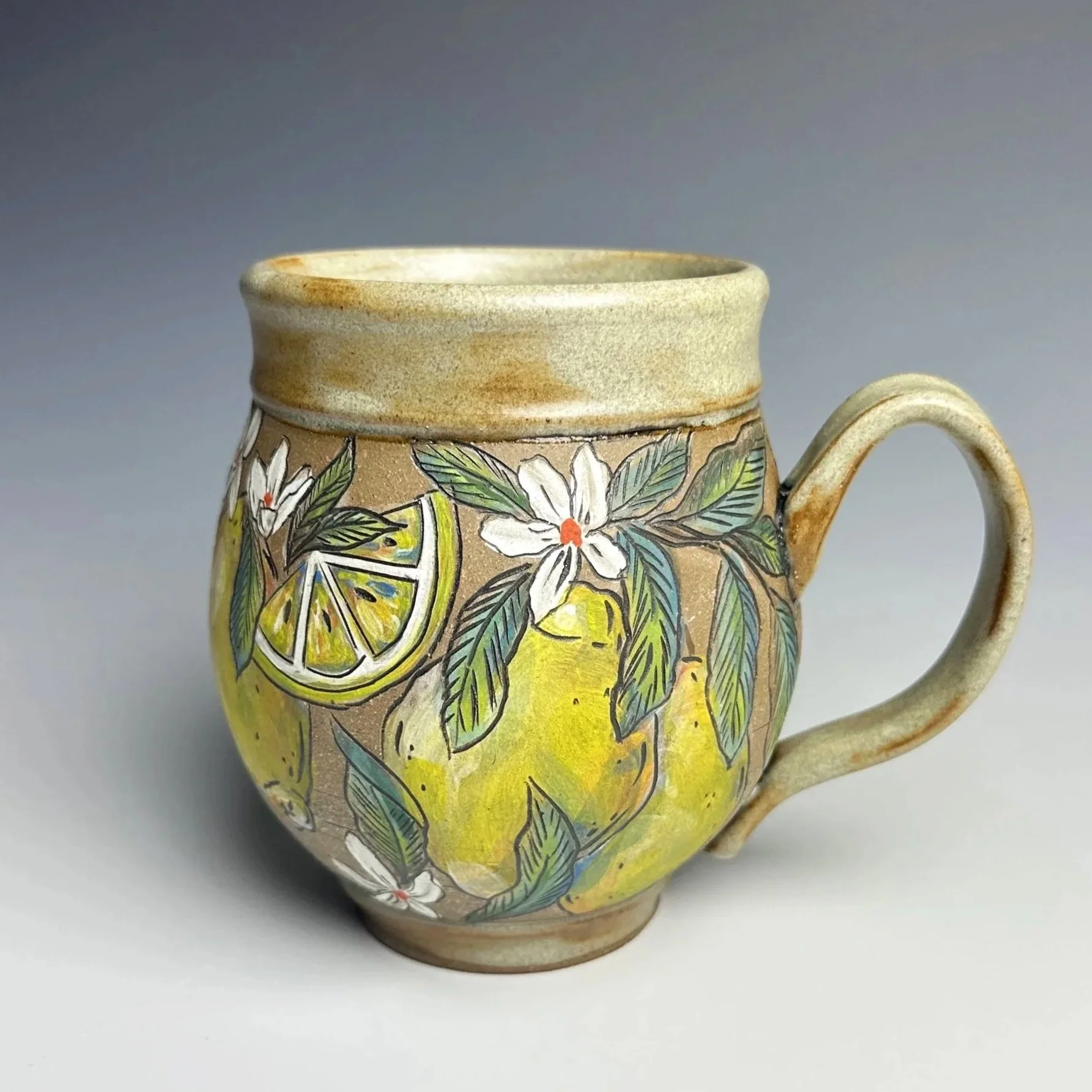 Two stacked ceramic mugs with colorful fruit and floral designs, featuring lemons and oranges with green leaves on a wooden background.