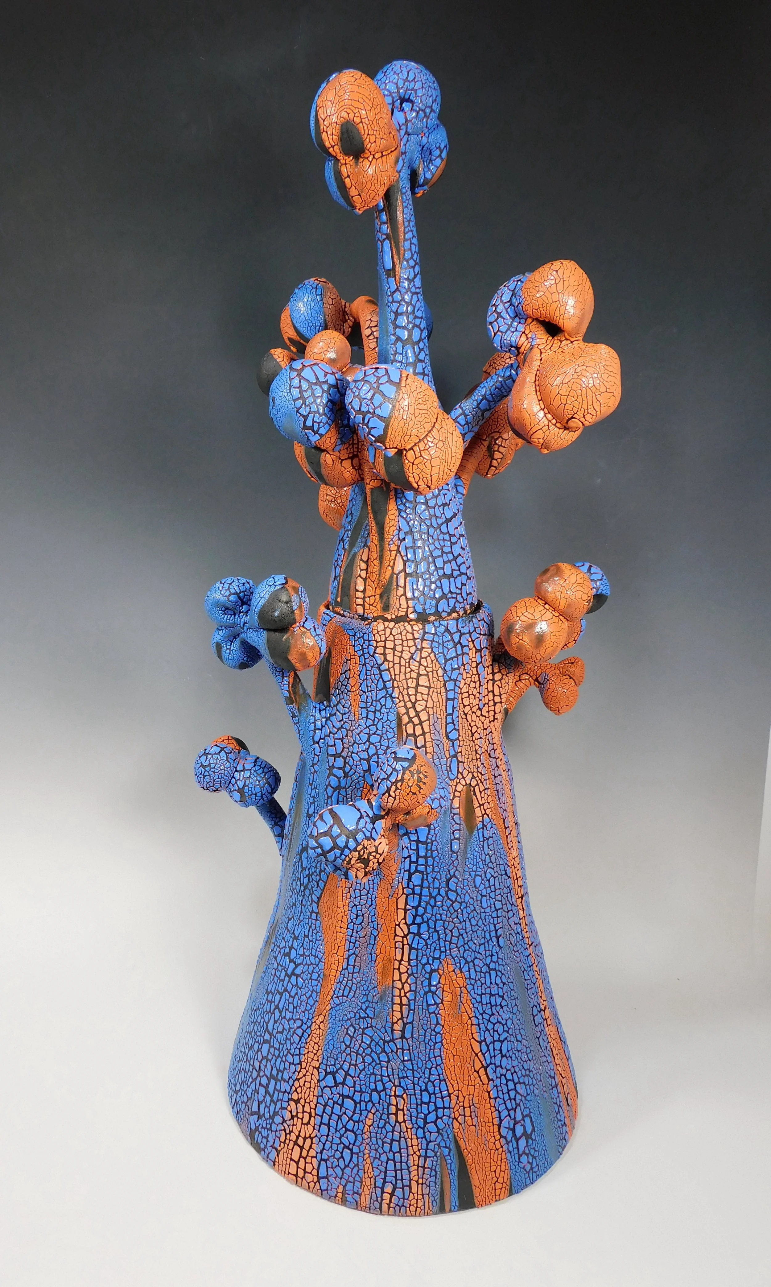 A colorful ceramic sculpture of a cactus with orange and blue cracked glaze pattern against a dark gradient background.