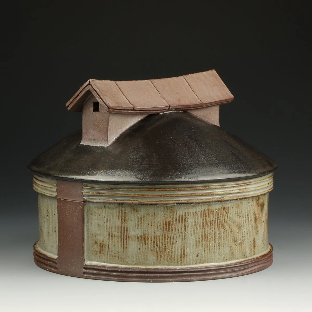 A ceramic teapot shaped like a small house with a brown roof and black base, and a rectangular body with a textured, striped pattern.