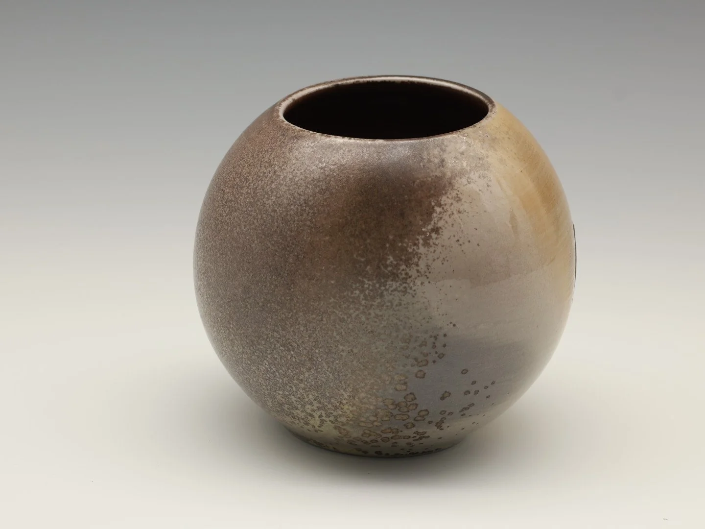 A round ceramic vase with a smooth, mottled brown and beige glaze, set against a plain gray background.