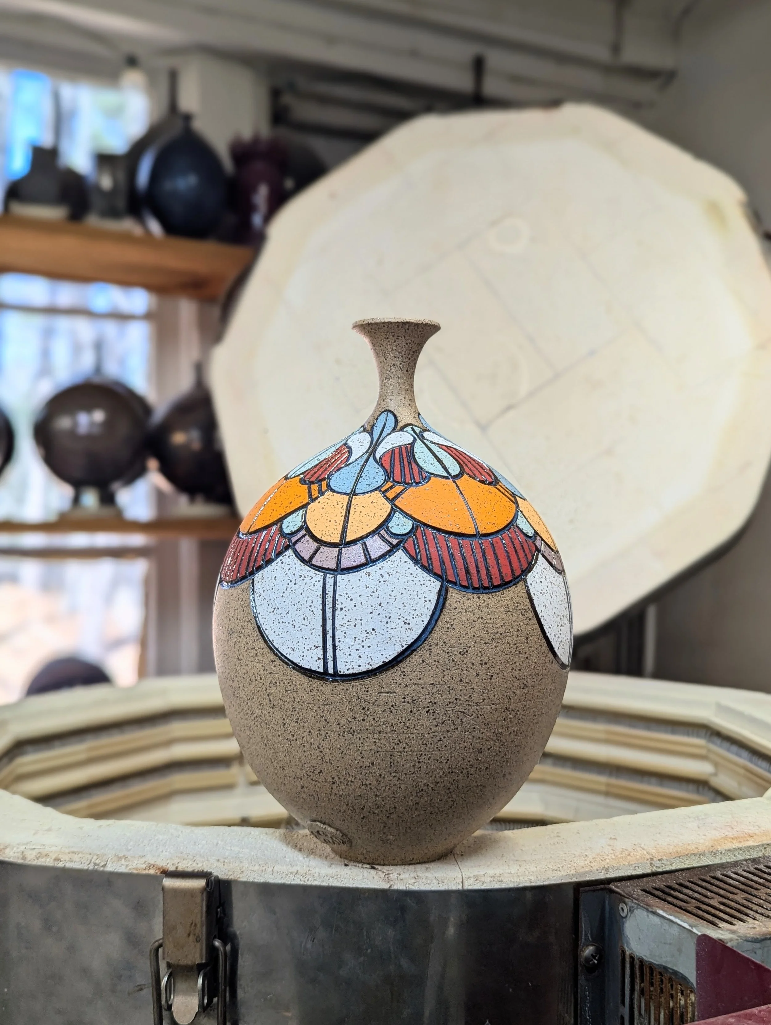 Decorative ceramic vase with colorful floral pattern on a display in a pottery studio.