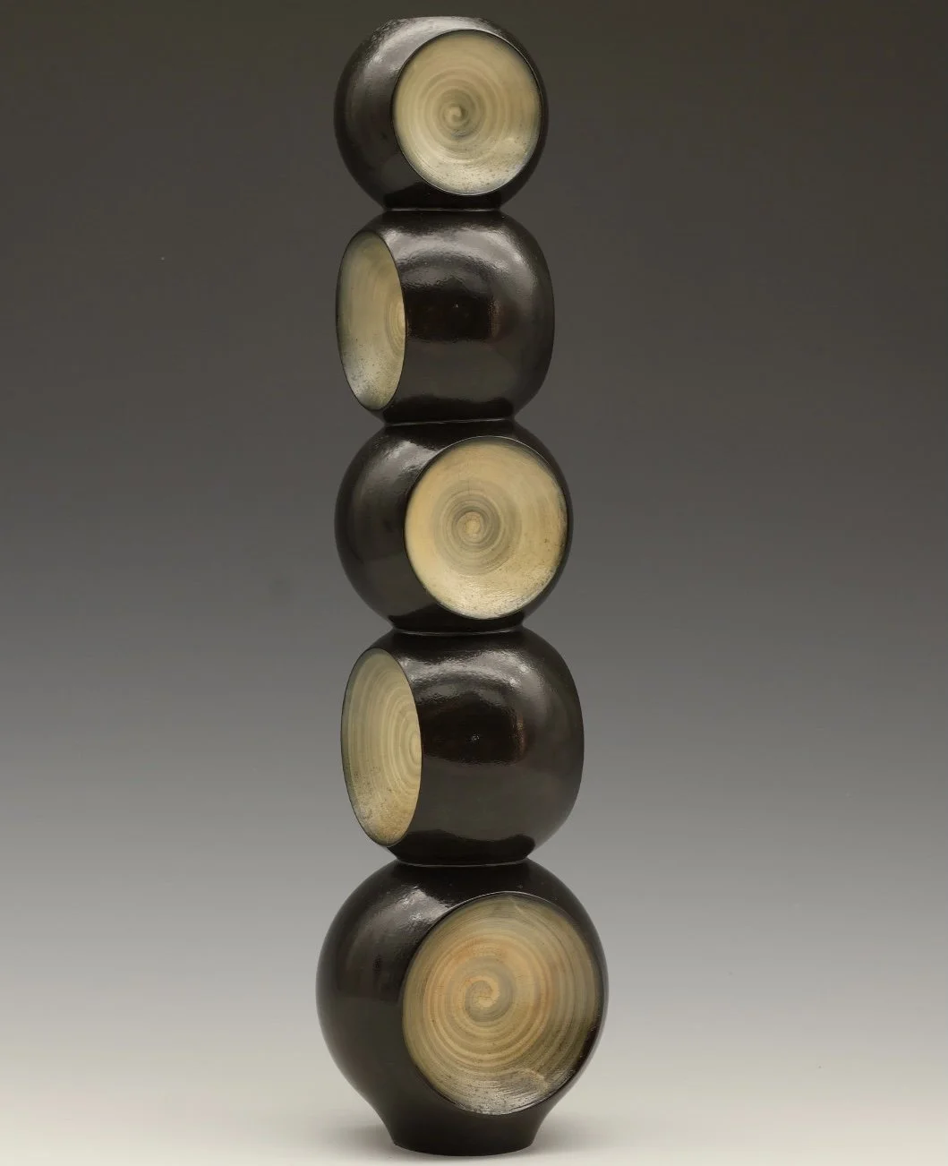 A vertical stack of five black circular objects with beige spiral patterns in the center, reflecting on a smooth surface against a gradient gray background.