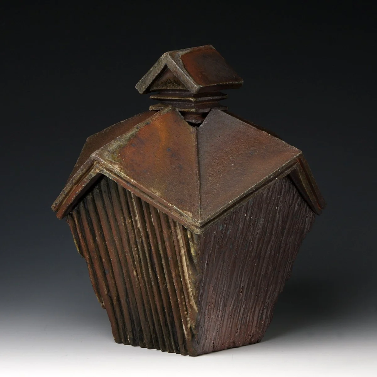 A sculpture resembling a house with a rusted metal roof and textured wooden walls, with a small chimney on top.