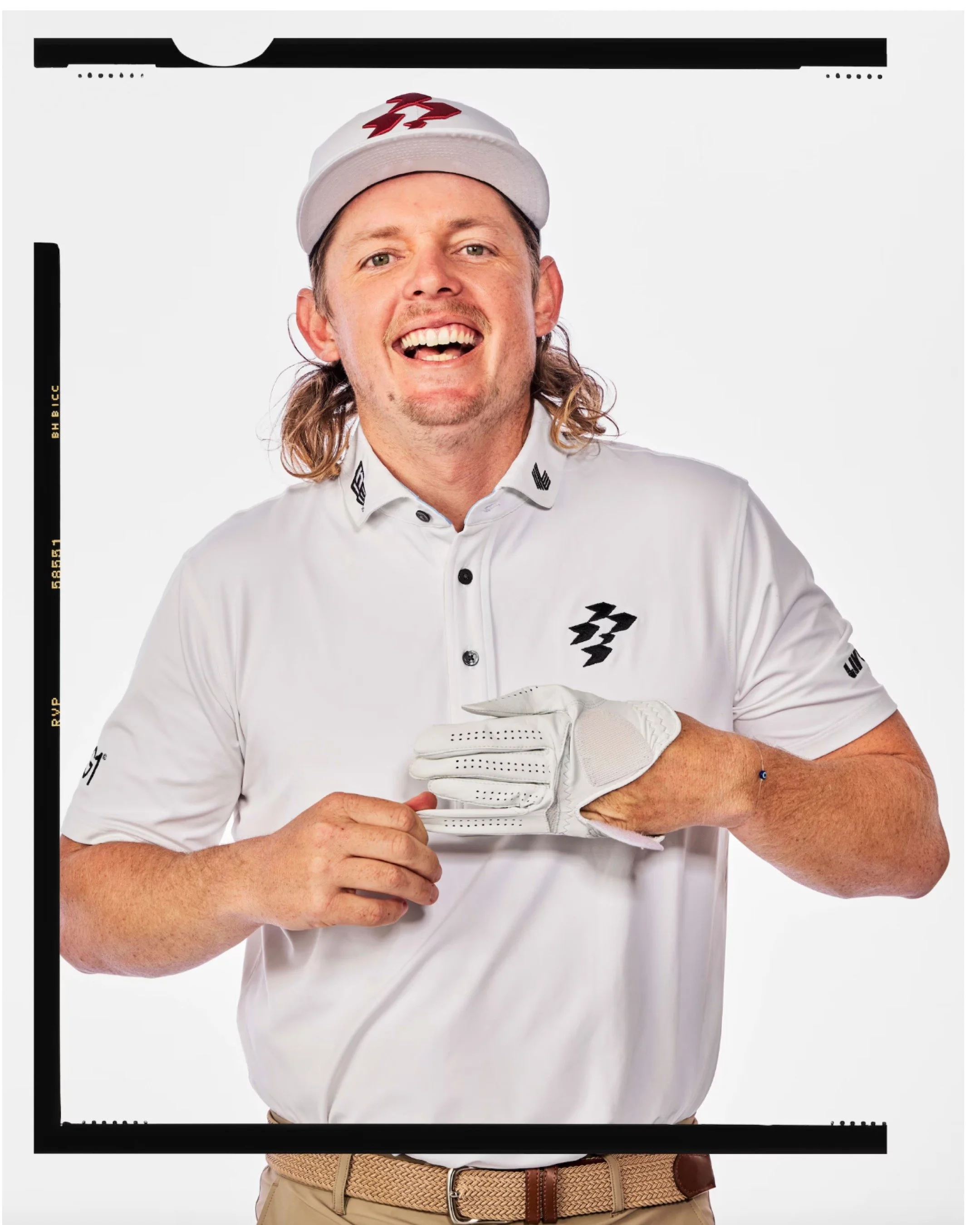 A man dressed in a white golf shirt and cap, holding a golf glove, smiling at the camera.