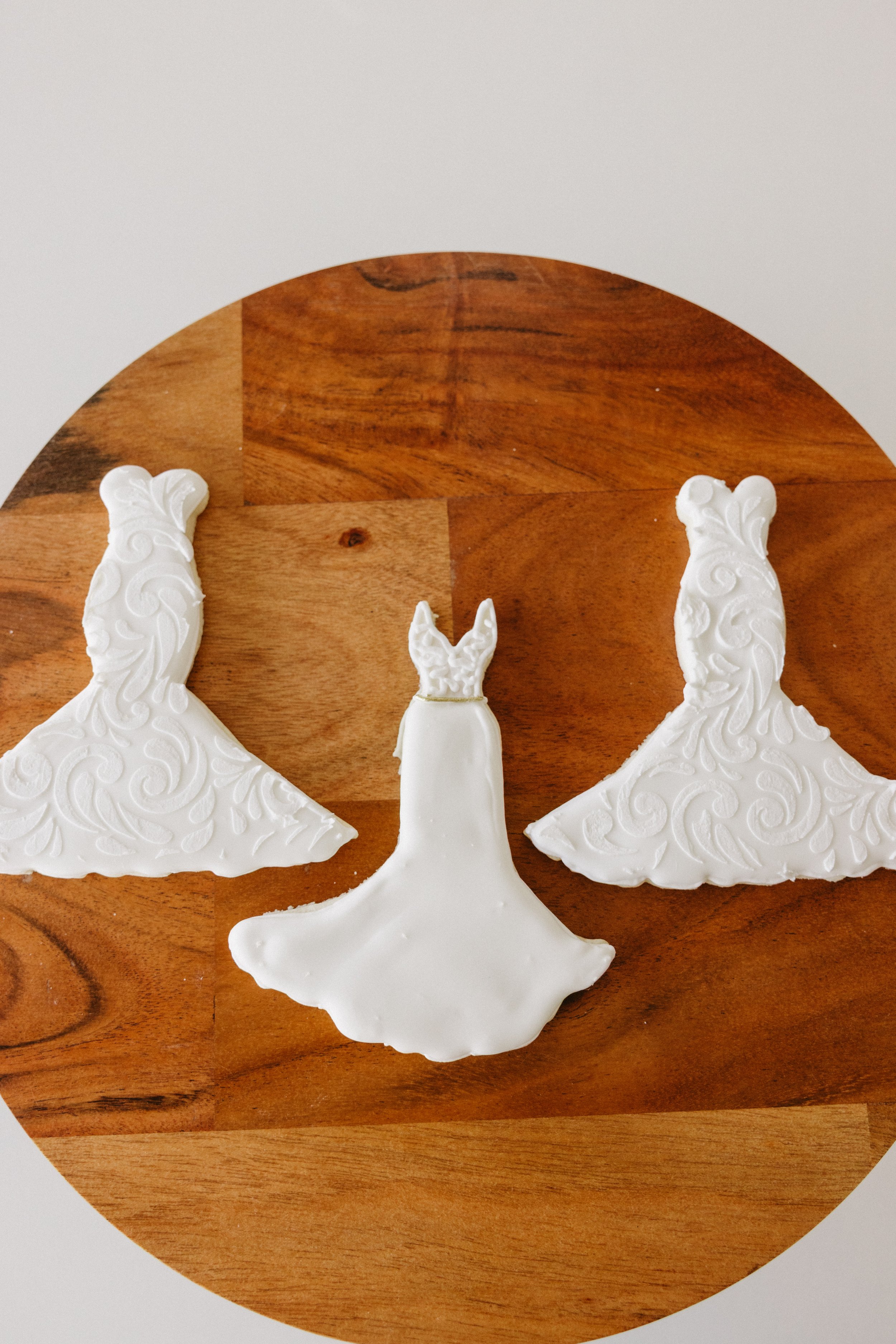 Three white dress-shaped cookies with textured icing, arranged on a wooden surface.