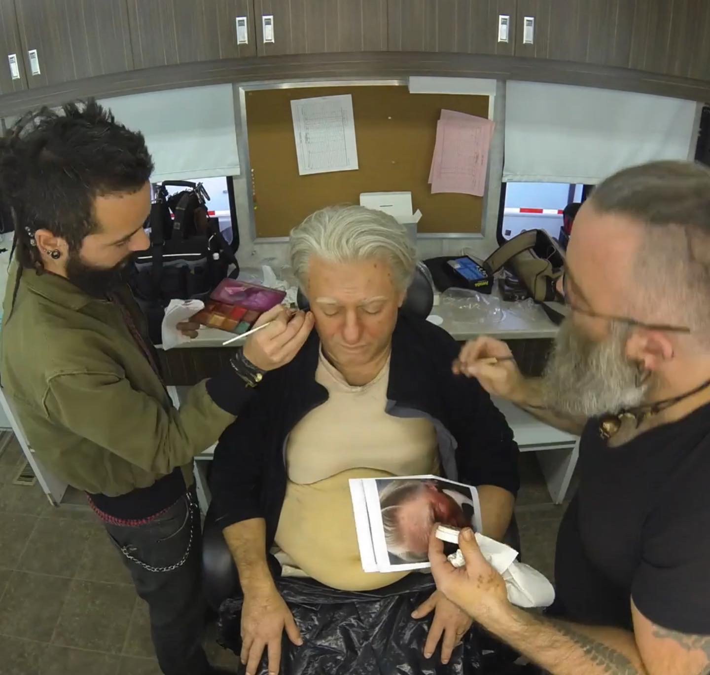 Trois personnes dans un salon de maquillage, l'une assise tandis que les deux autres appliquent du maquillage professionnel sur elle.