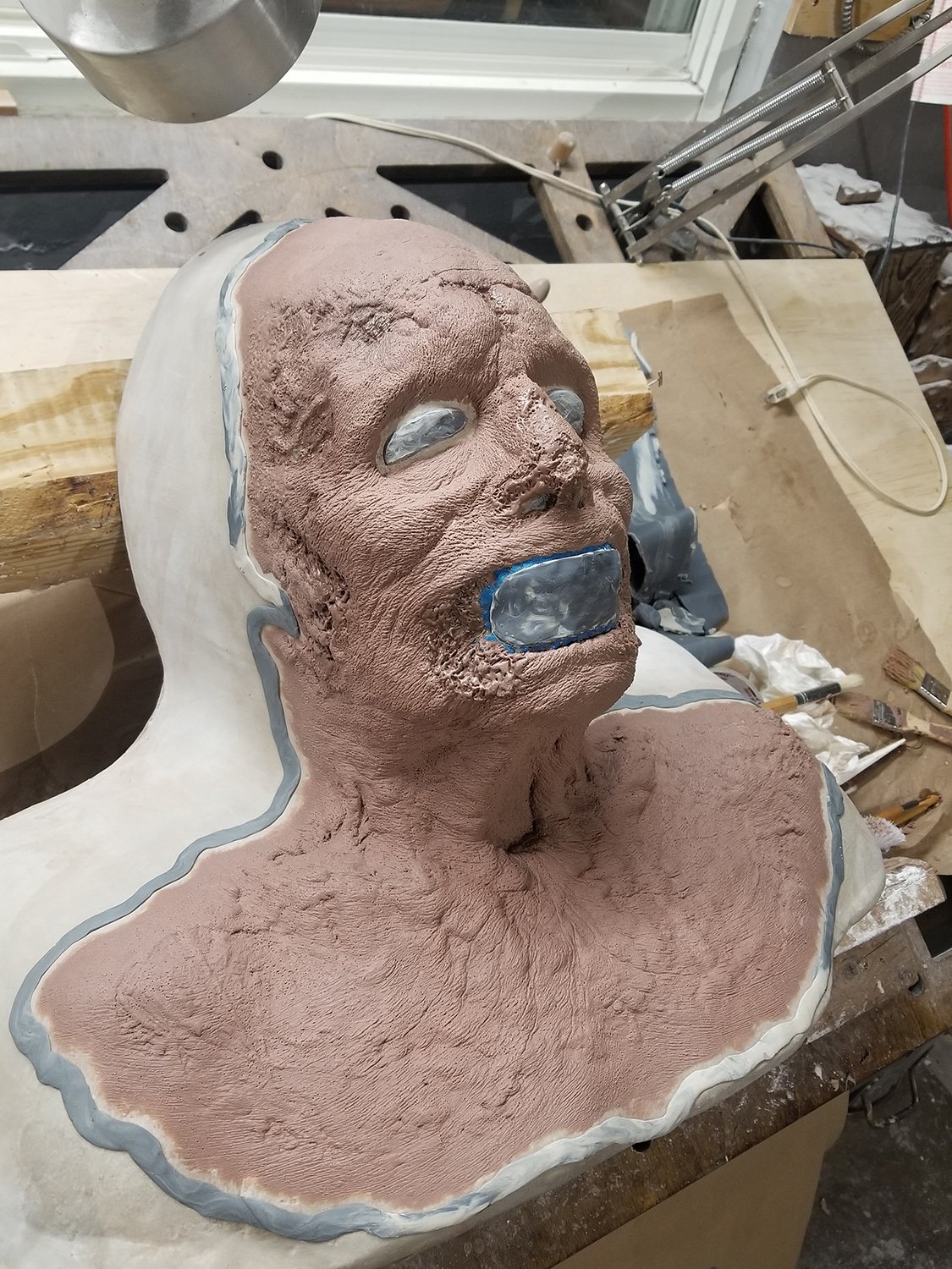Modèle de sculpture d'un buste humain en argile sur une table de travail avec des outils autour, en cours de création.