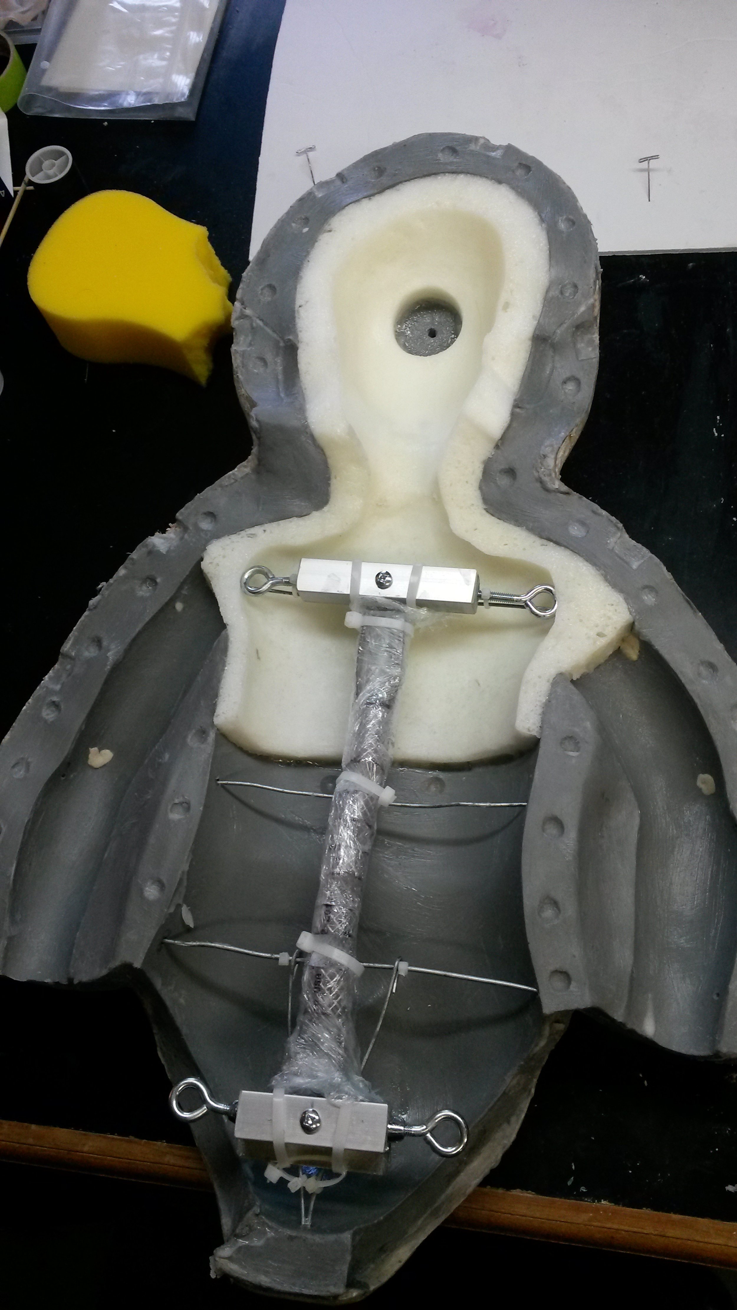 Prototype d'un moule en silicone avec des éléments en métal et mousse à l'intérieur, posés sur une surface noire.