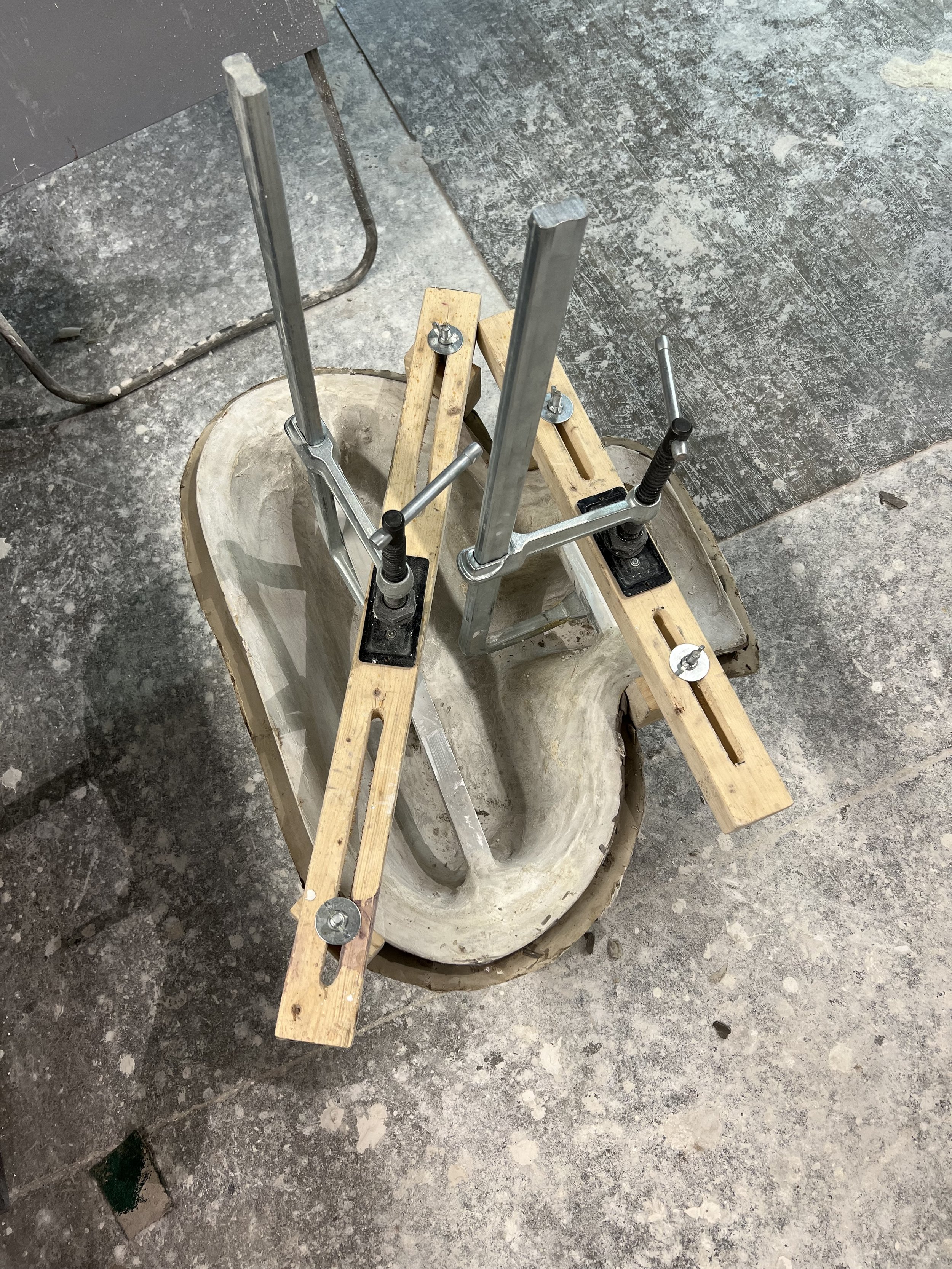 Un moule en plâtre sur le sol avec des supports en métal et bois fixés dessus.