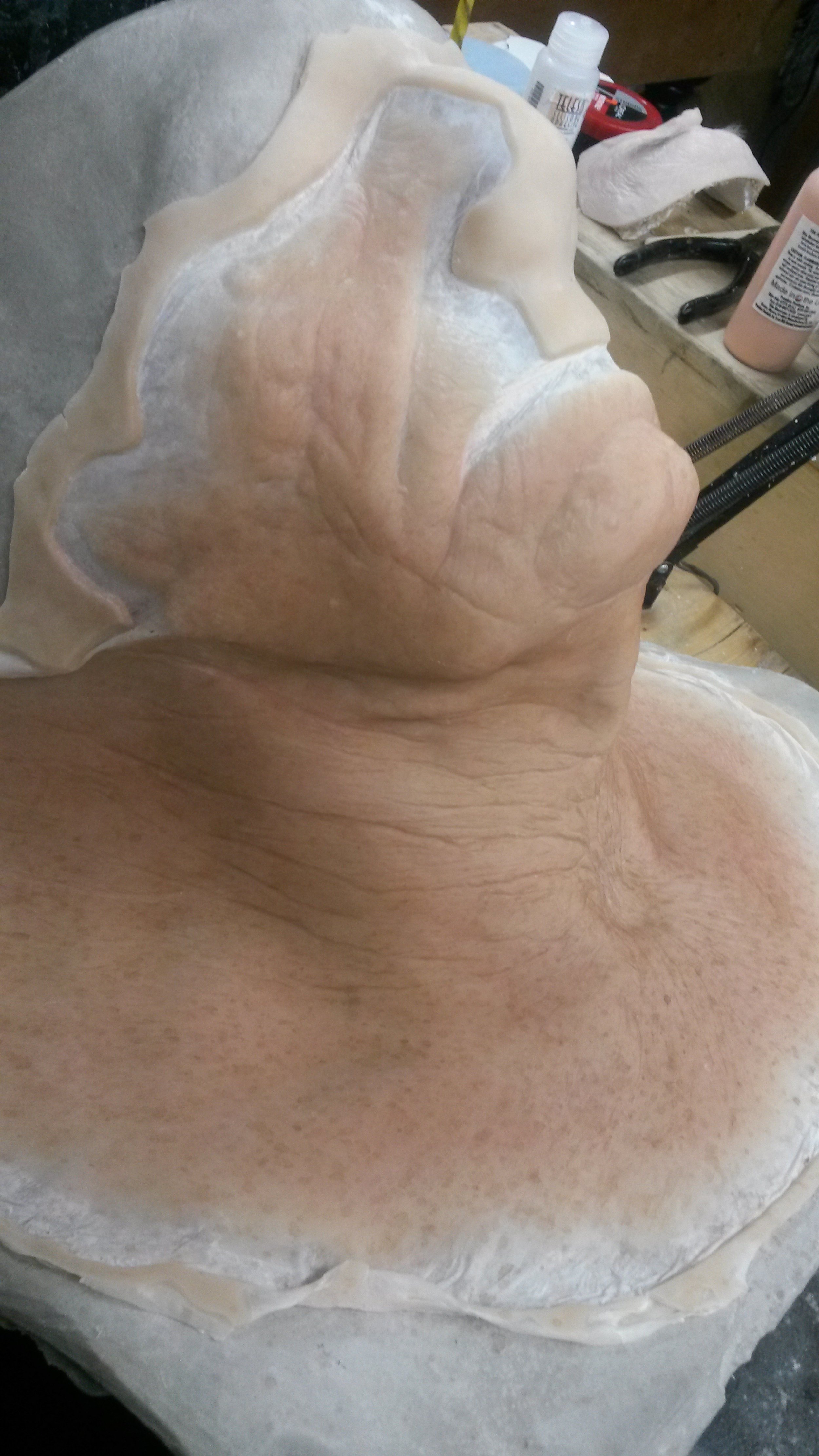 Prothèse en silicone pour le visage et le cou sur une table d'atelier, avec des outils et des produits à l'arrière-plan.