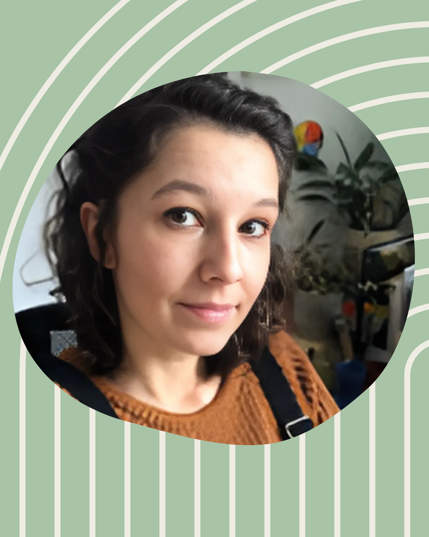 Junge Frau vor grünem Hintergrund mit Pflanzen und buntem Papagei im Hintergrund. Sie trägt einen braunen Pullover und schaut in die Kamera.