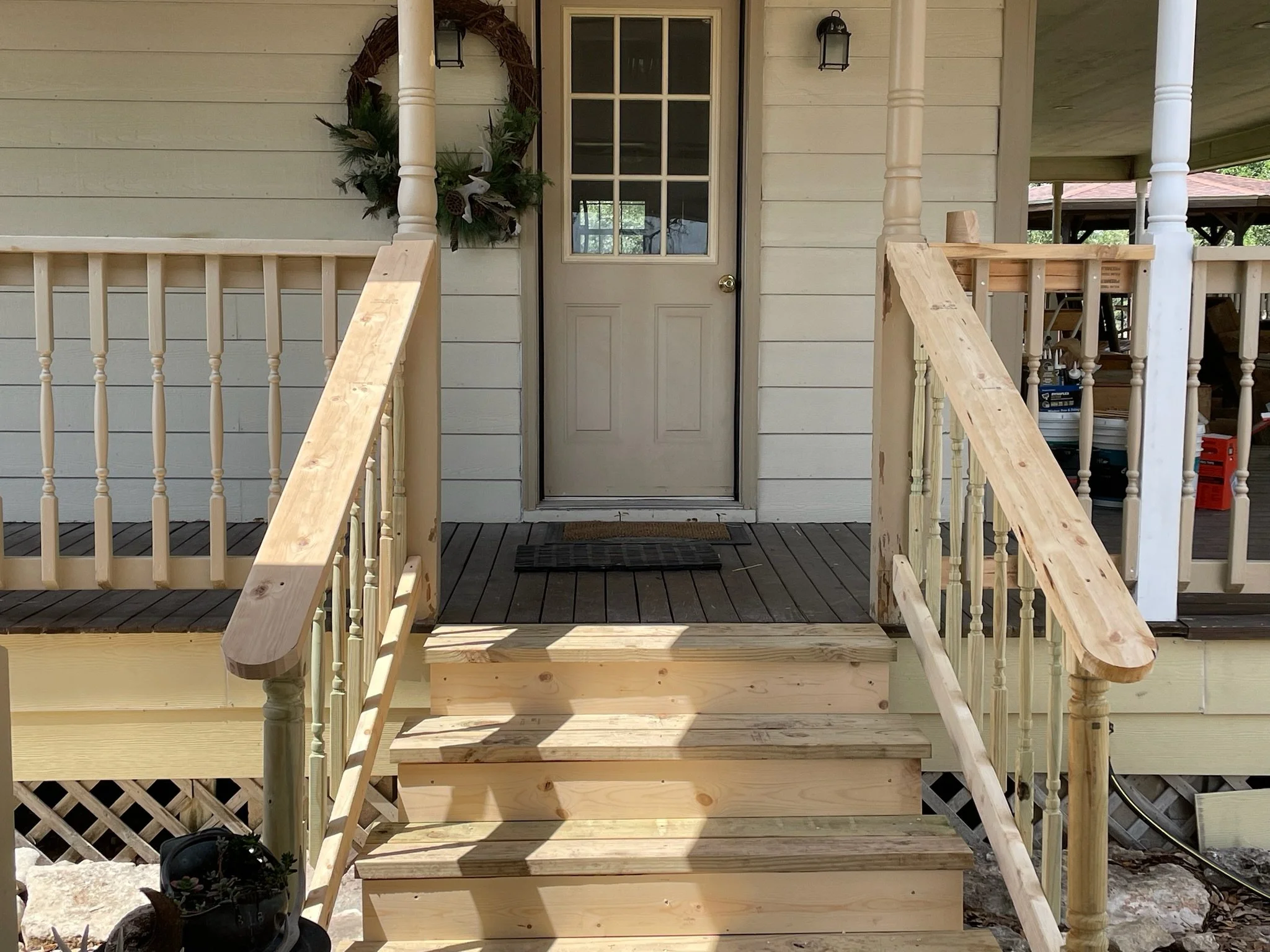 Wooden front steps and porch railing leading up to a door with windowpanes, decorated with a wreath, on a house with beige siding.