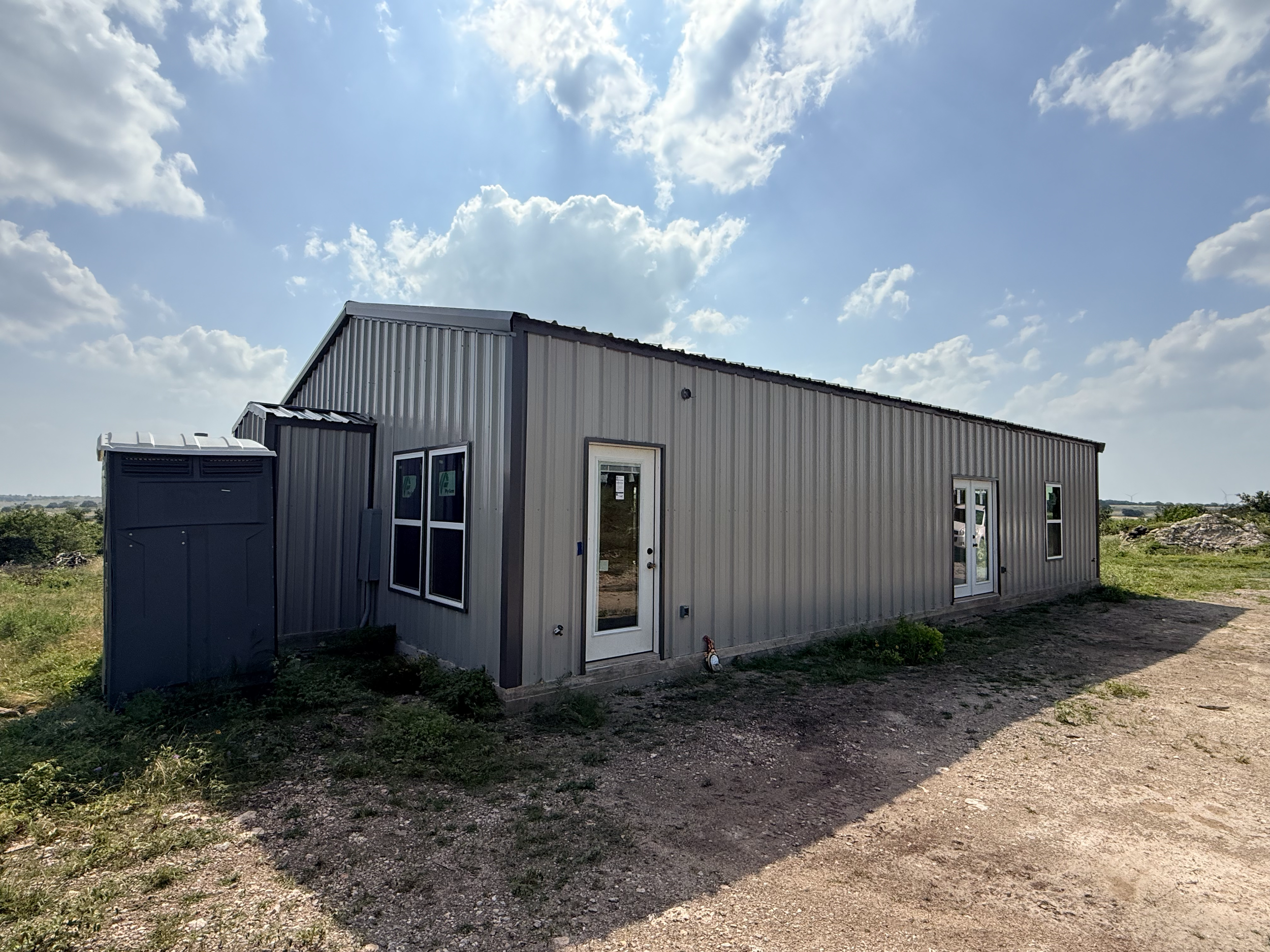A small metal building under a partly cloudy sky with scattered clouds and sunlight.
