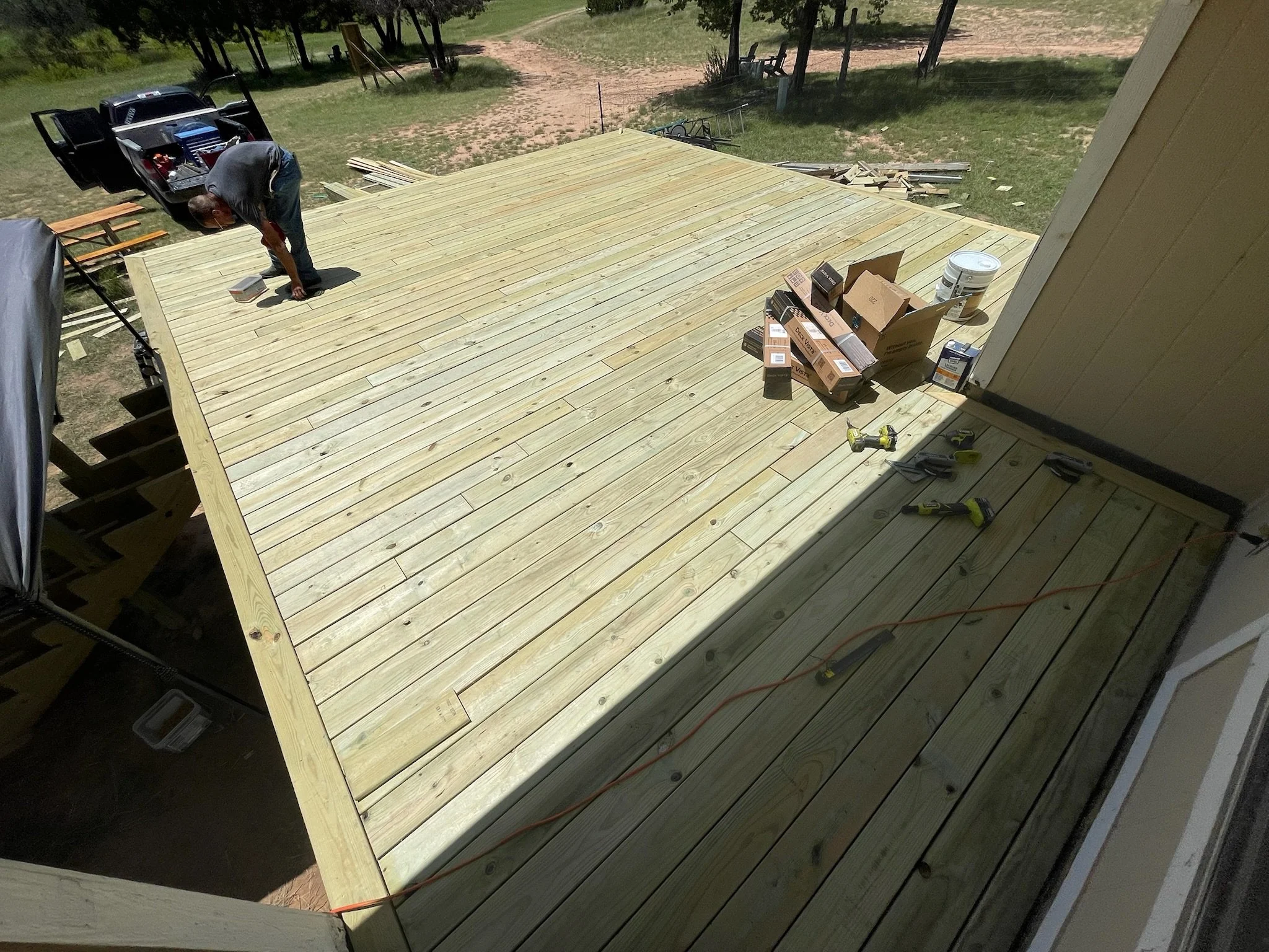 Person working on building a large wooden deck attached to a house, with tools and materials scattered around.