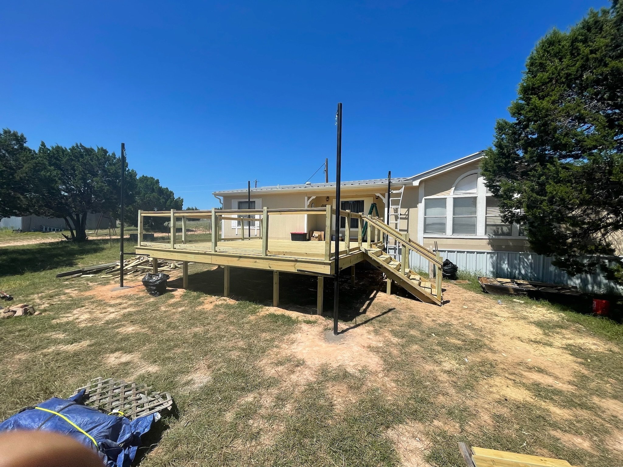 A house with a new wooden deck under construction, surrounded by trees and blue sky.