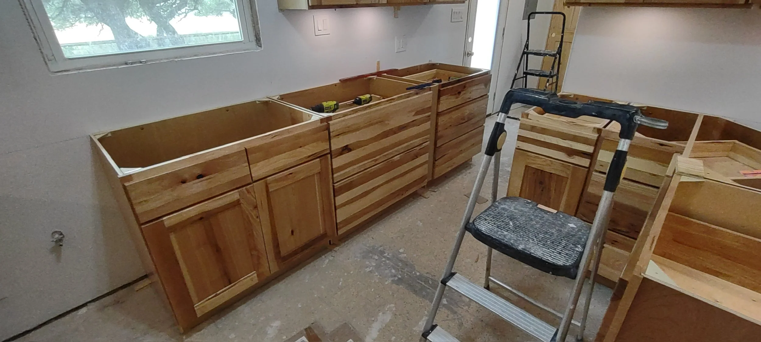 Building new wooden cabinets in a room under construction, with a window on the wall and construction tools nearby.