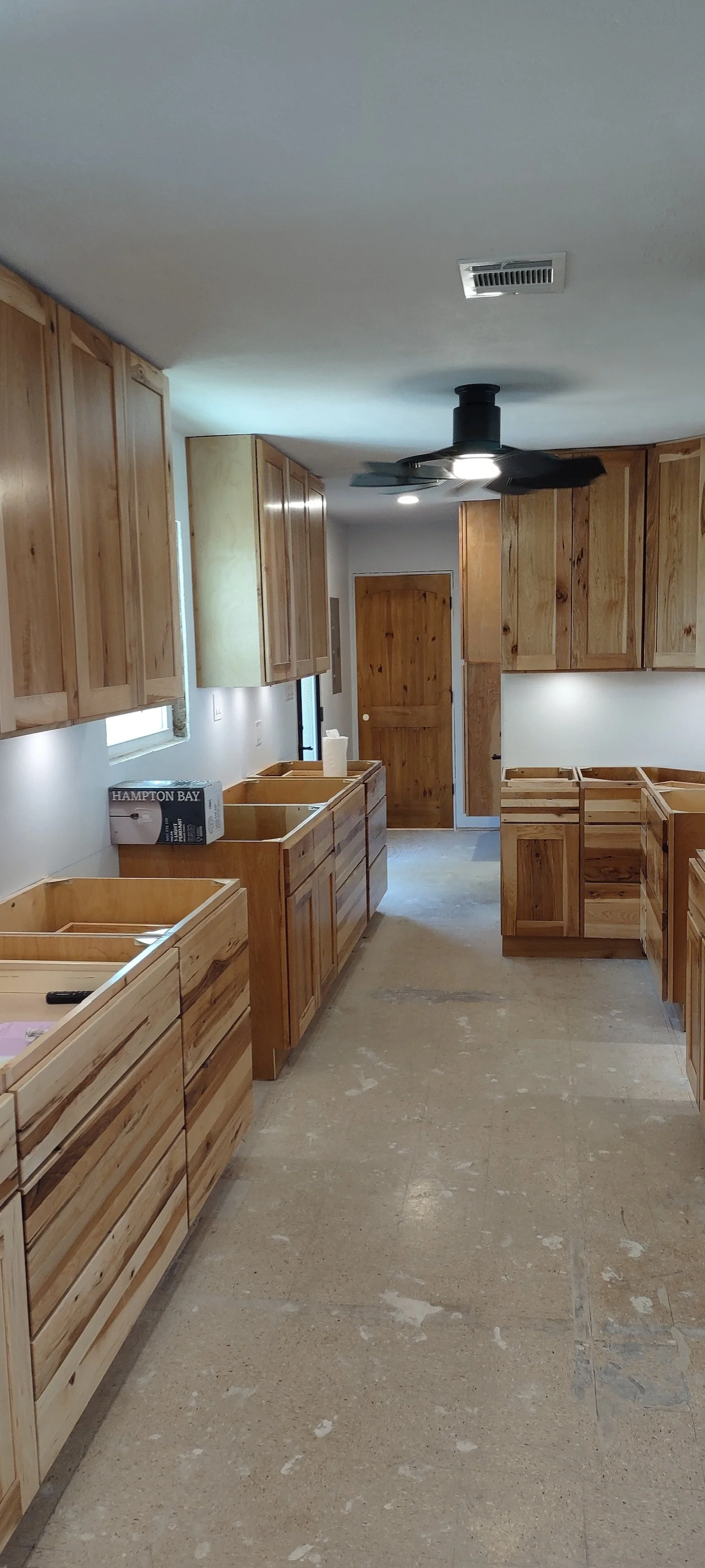 Kitchen under construction with unfinished wooden cabinets and a ceiling fan
