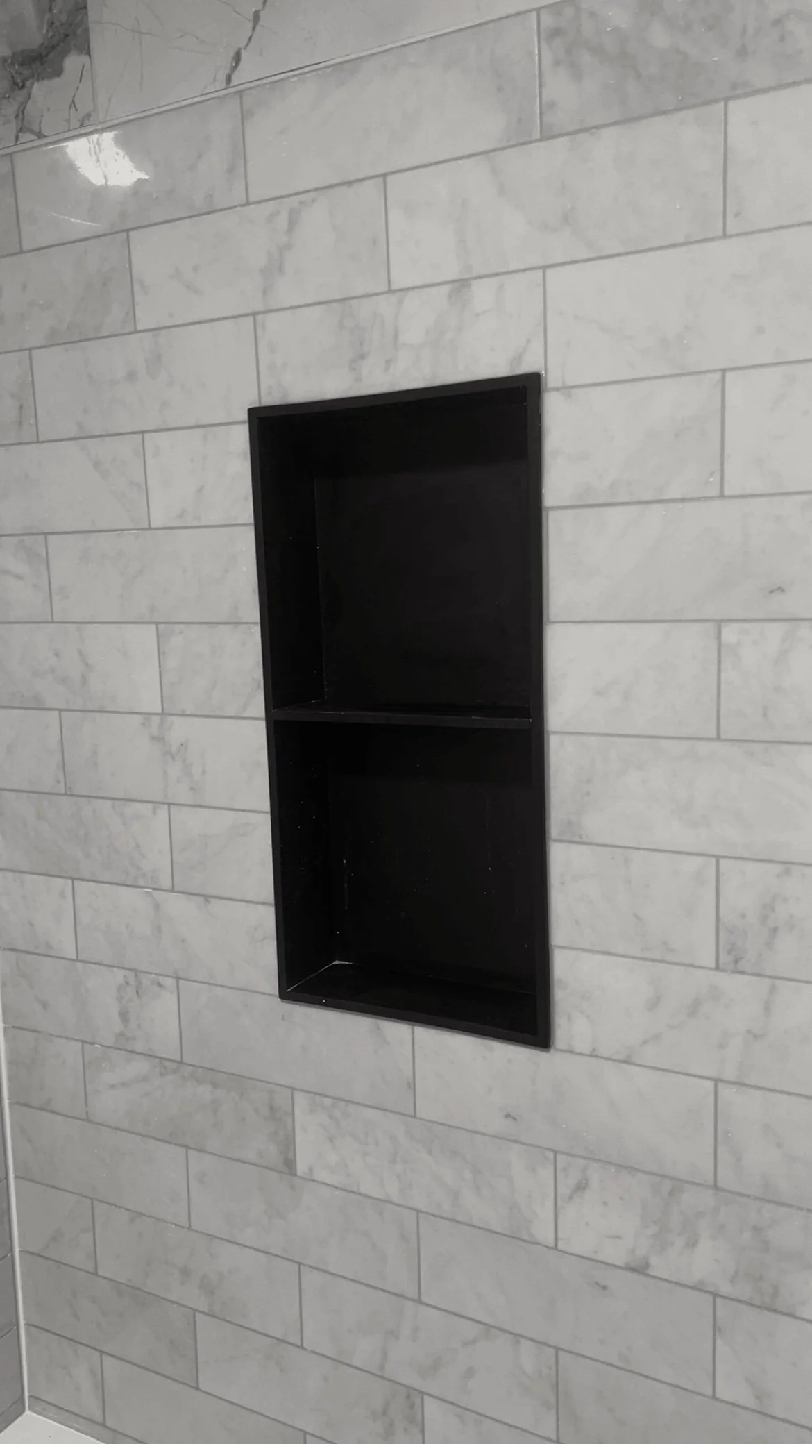Empty black wall-mounted shelf on light gray marble tile wall.