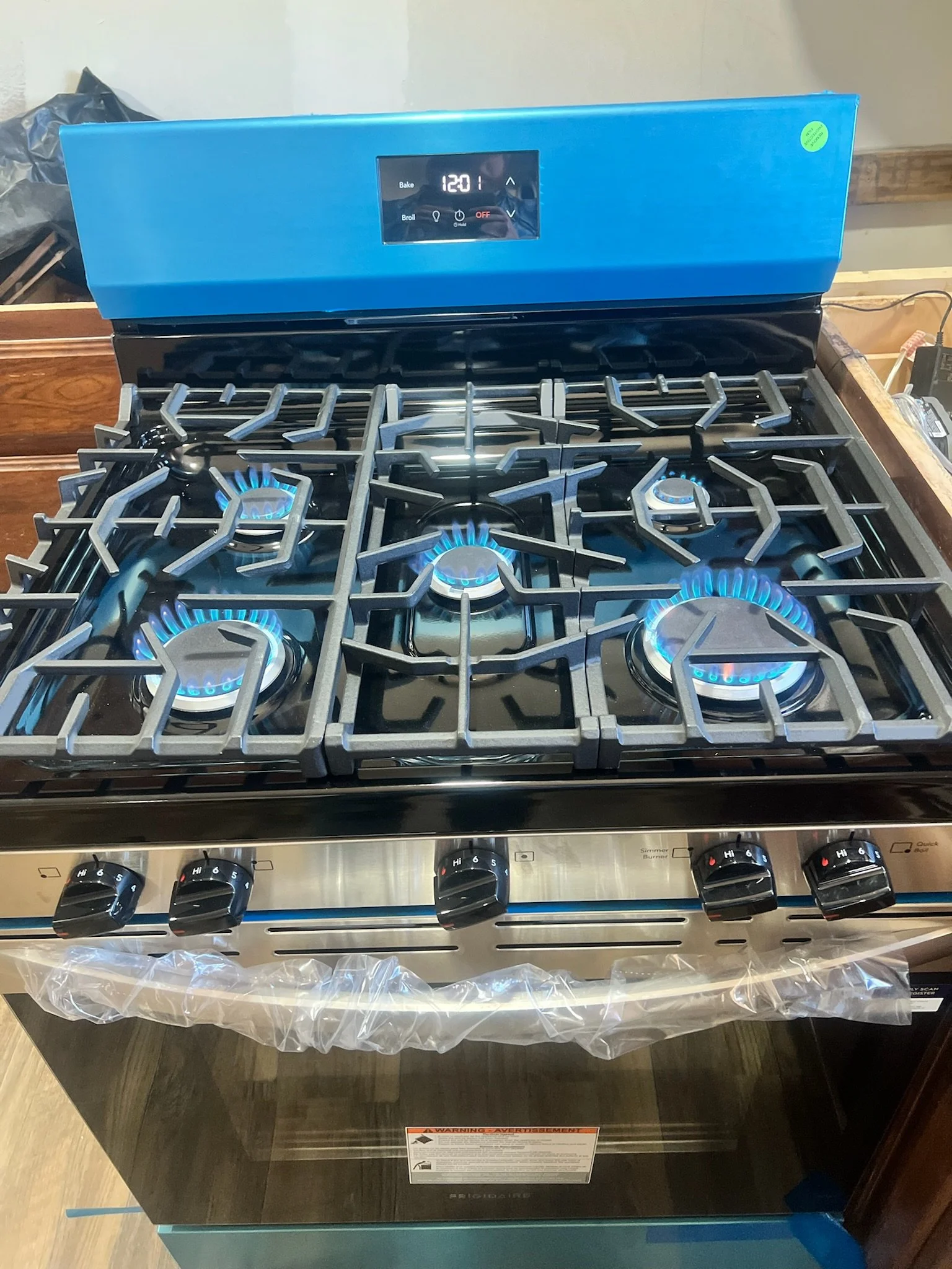 A modern gas stove with four lit burners, metallic grates, control knobs, and a digital display on the back panel.