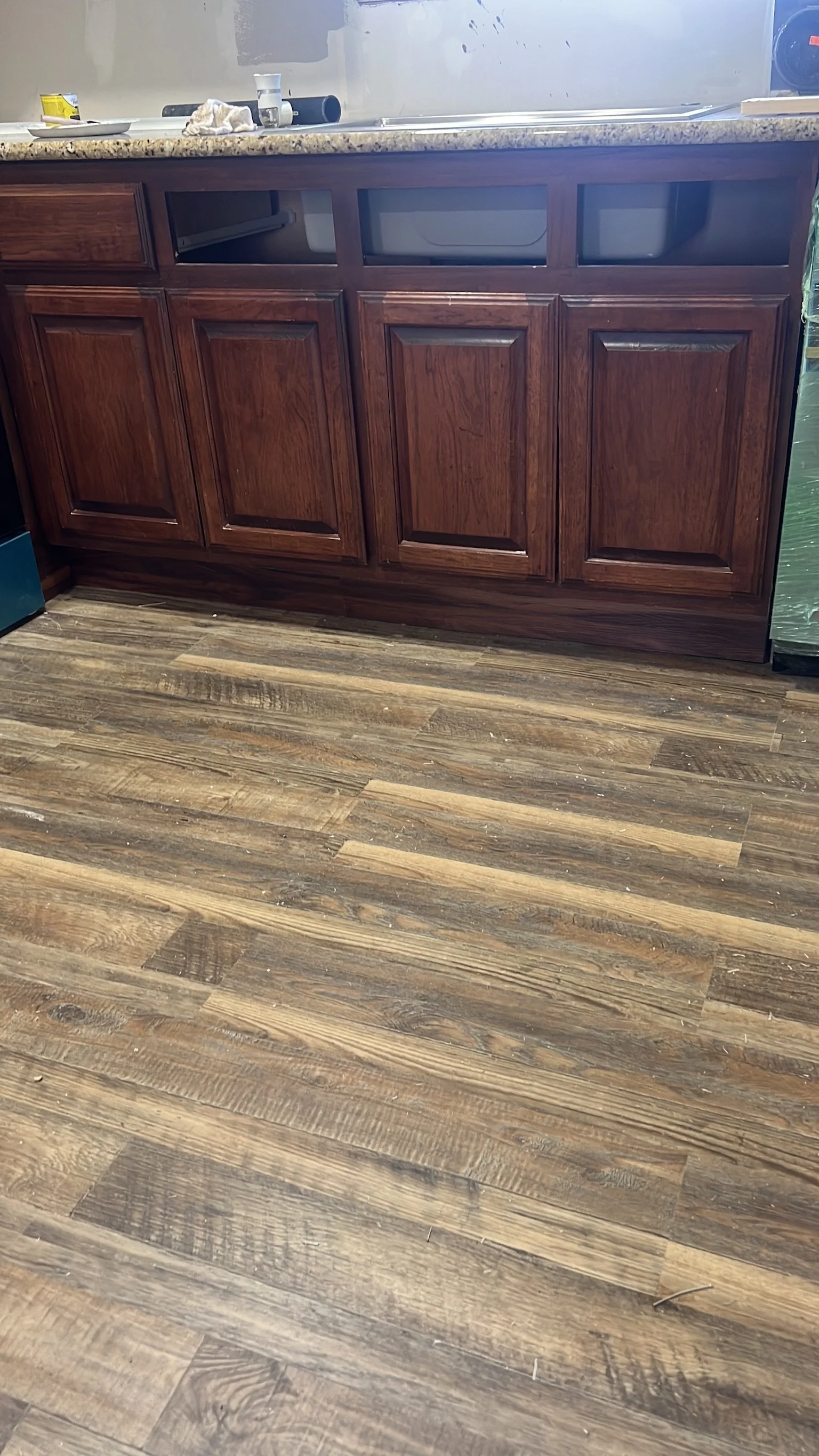 Kitchen counter with clutter, including a cup, a towel, and containers, with partially painted wall and wood floor.