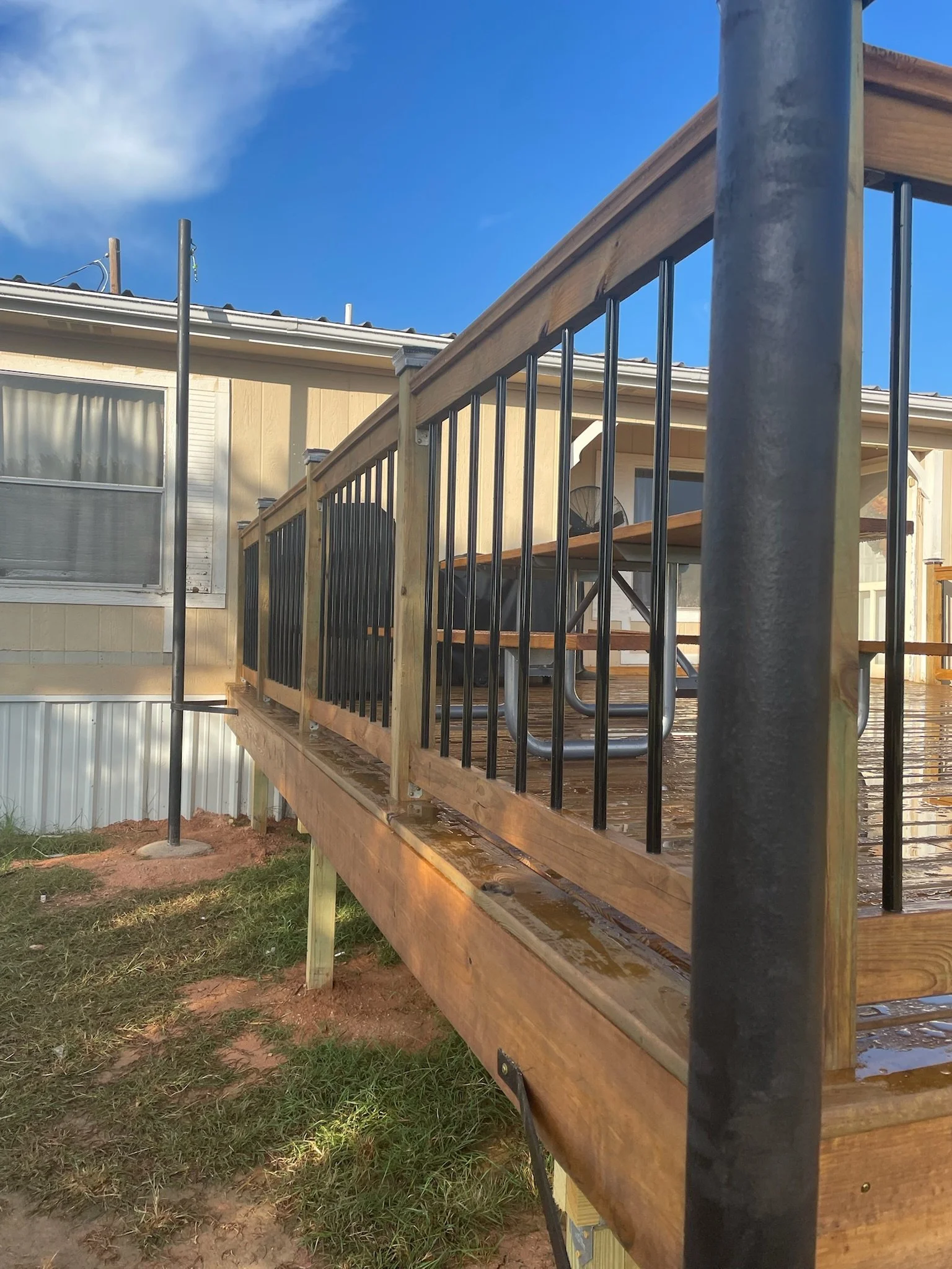 Backyard deck with wooden railings and metal balusters, a black metal pole, and a portion of a house with beige siding and a window.