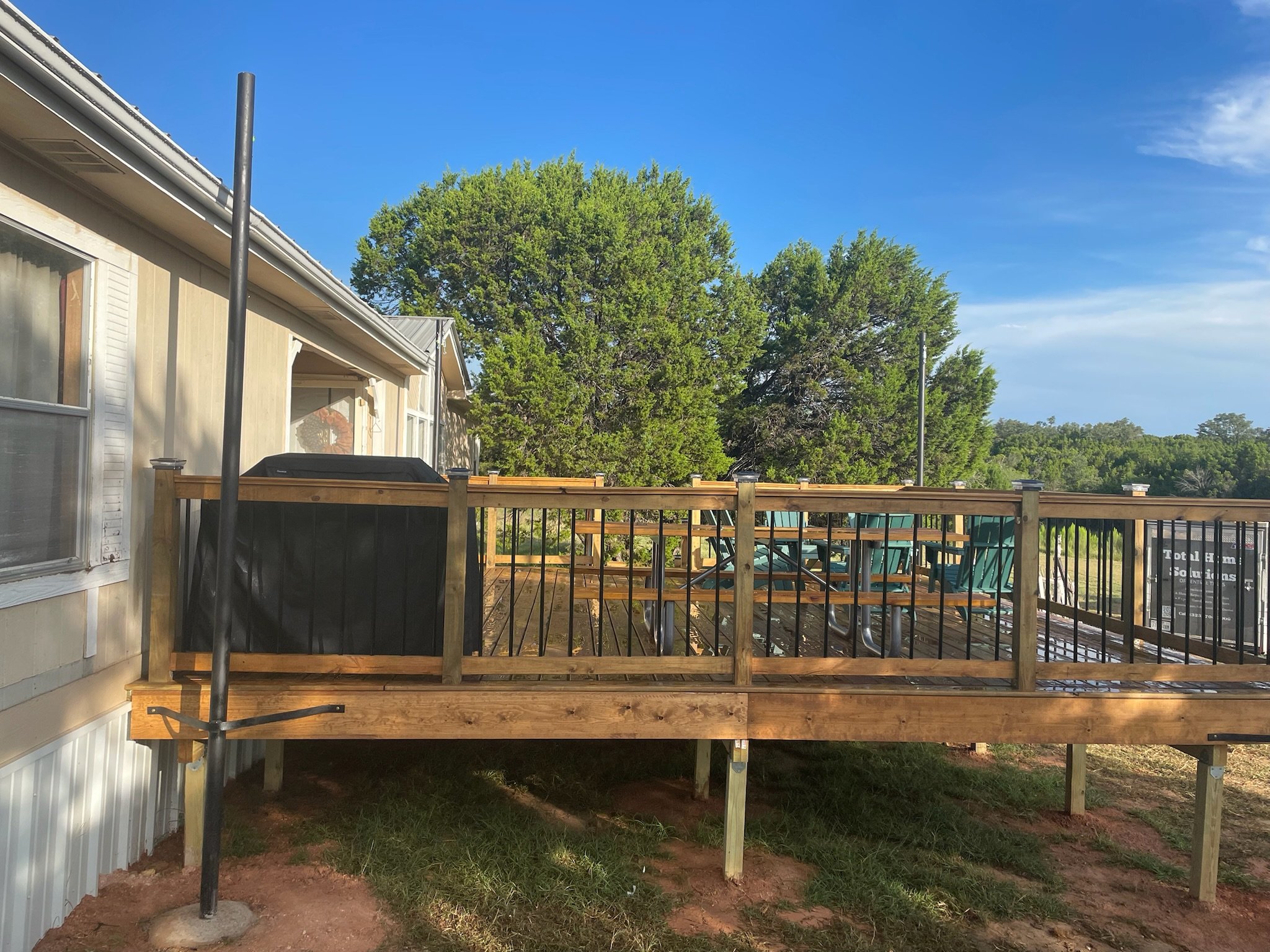 Backyard deck under construction with new wooden fencing and outdoor furniture, trees, and blue sky in the background.