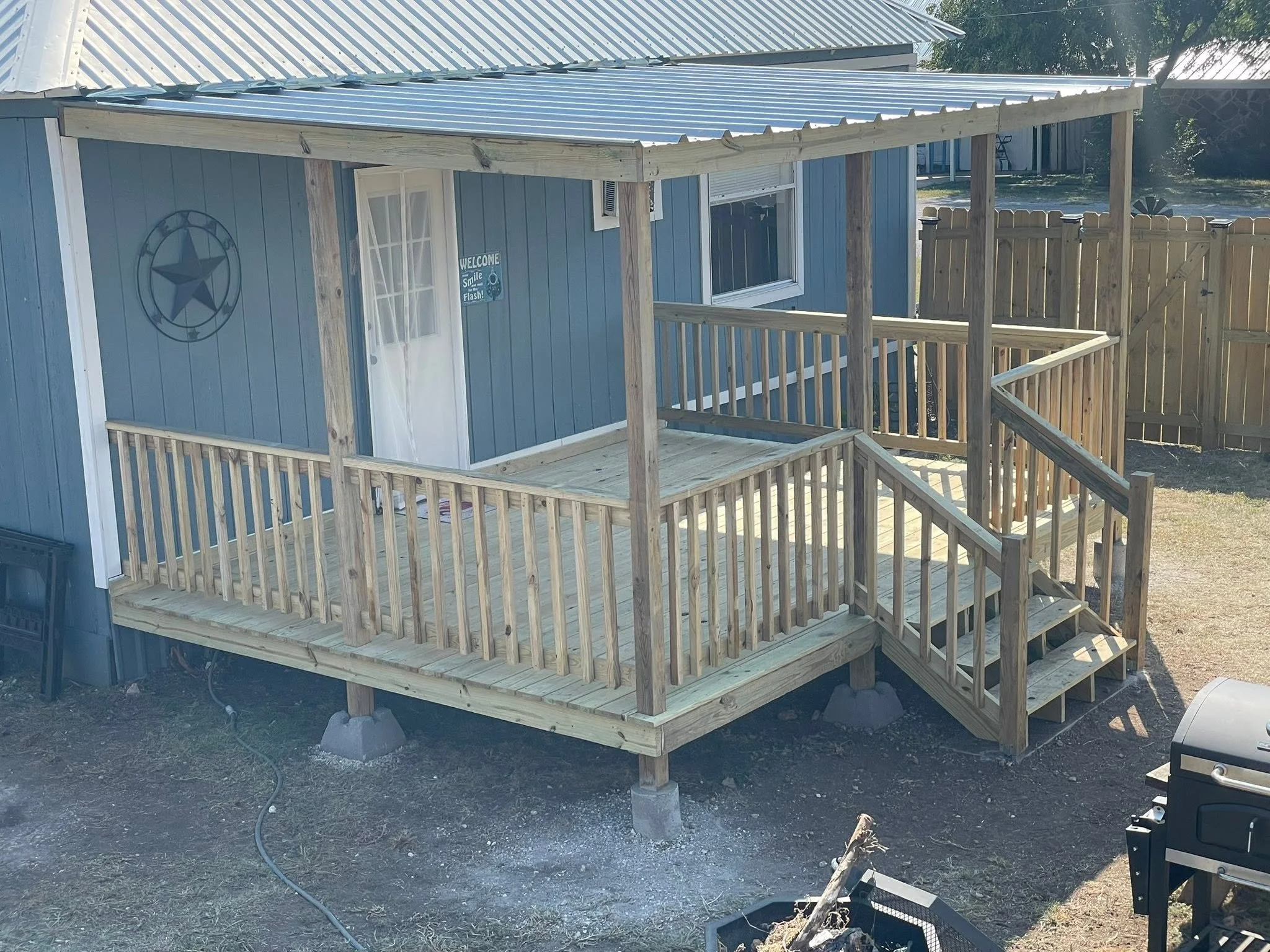 Newly constructed wooden deck attached to a blue house, surrounded by a wooden fence, with a star decoration on the house wall.
