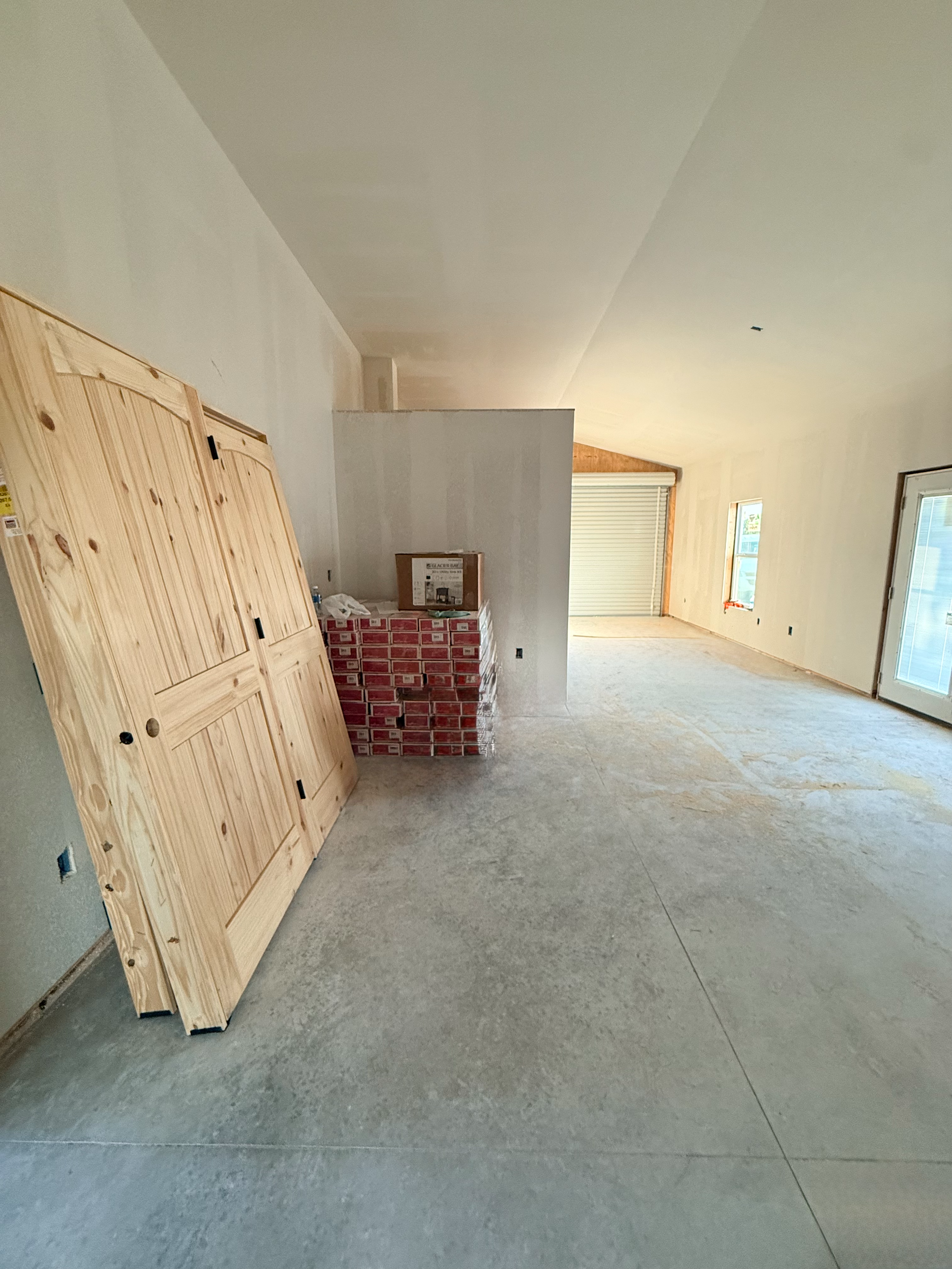 A room under construction with unfinished flooring, a stack of wooden doors leaning against a wall, and a brick heater in progress.