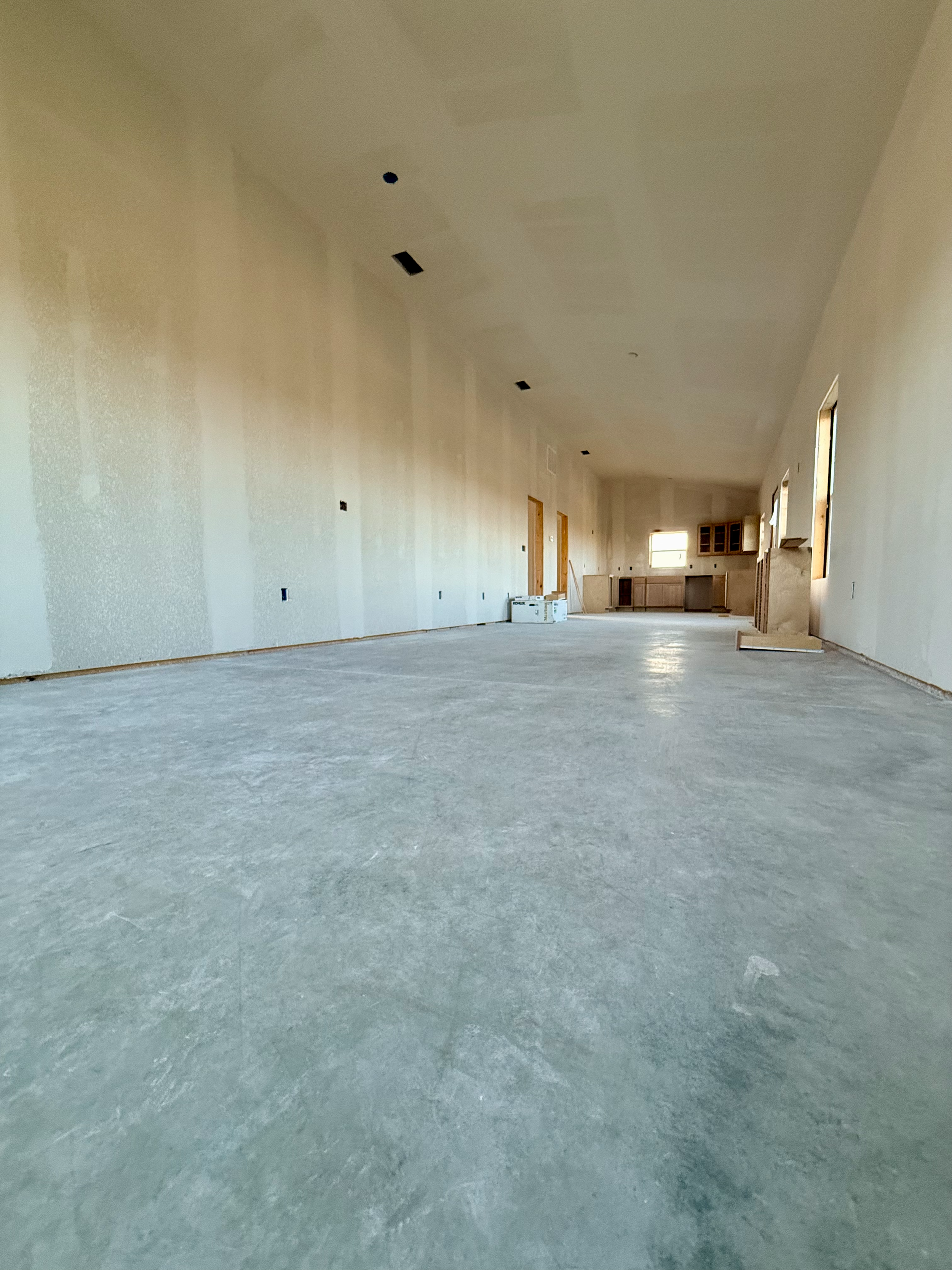 Empty room under construction with unfinished walls, ceiling, and concrete floor, with some construction materials and tools visible.