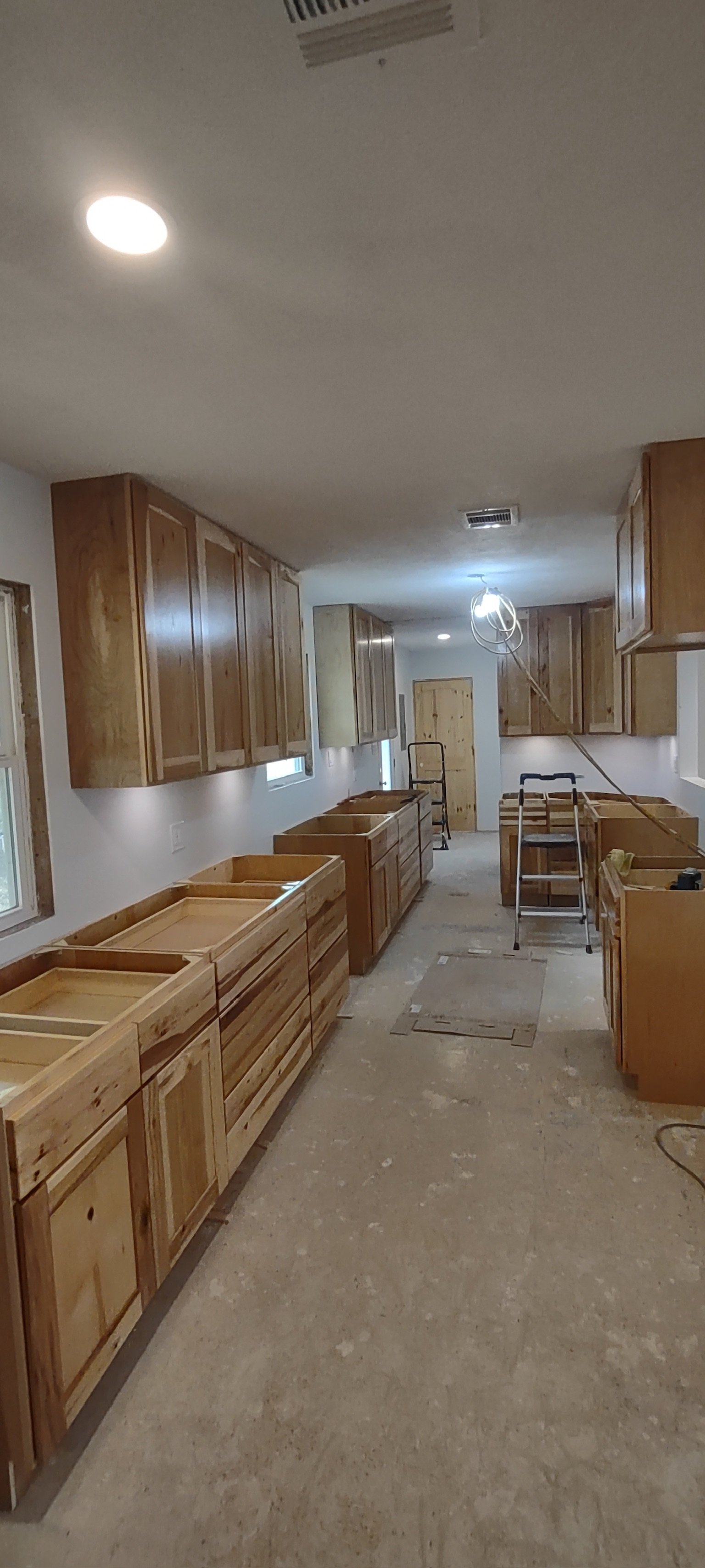 Kitchen under renovation with wooden cabinets, some not yet installed, and construction tools.
