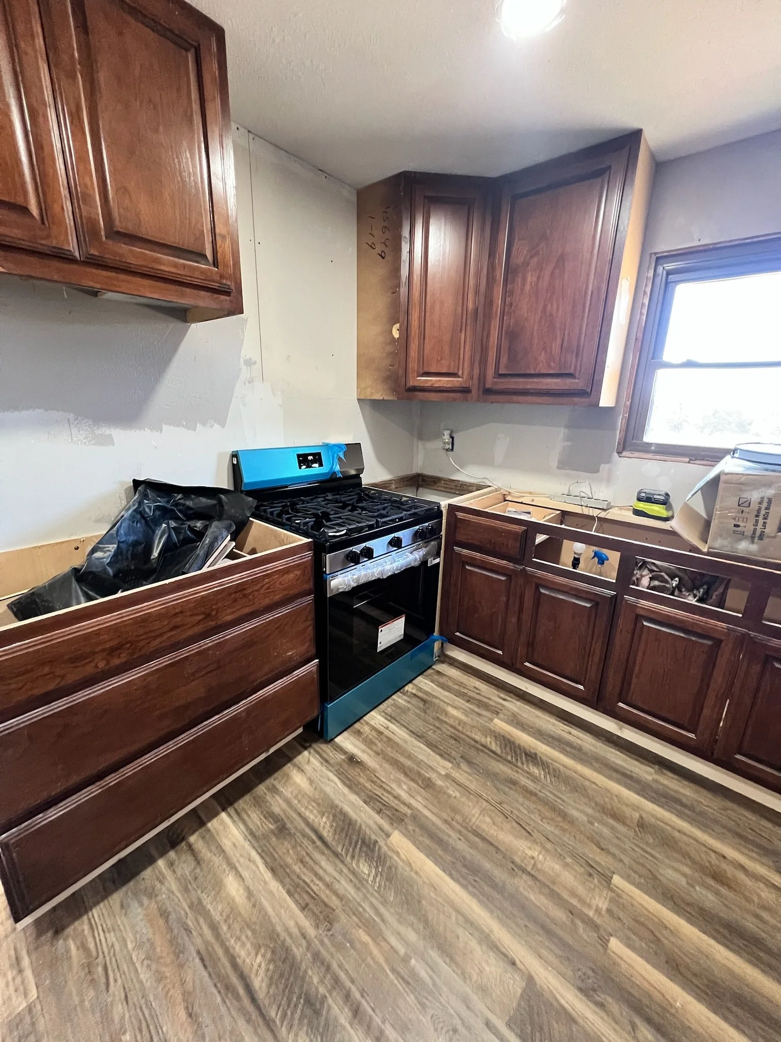 Kitchen with unfinished wooden cabinets, a stove, and a window, in the process of being remodeled or repaired.