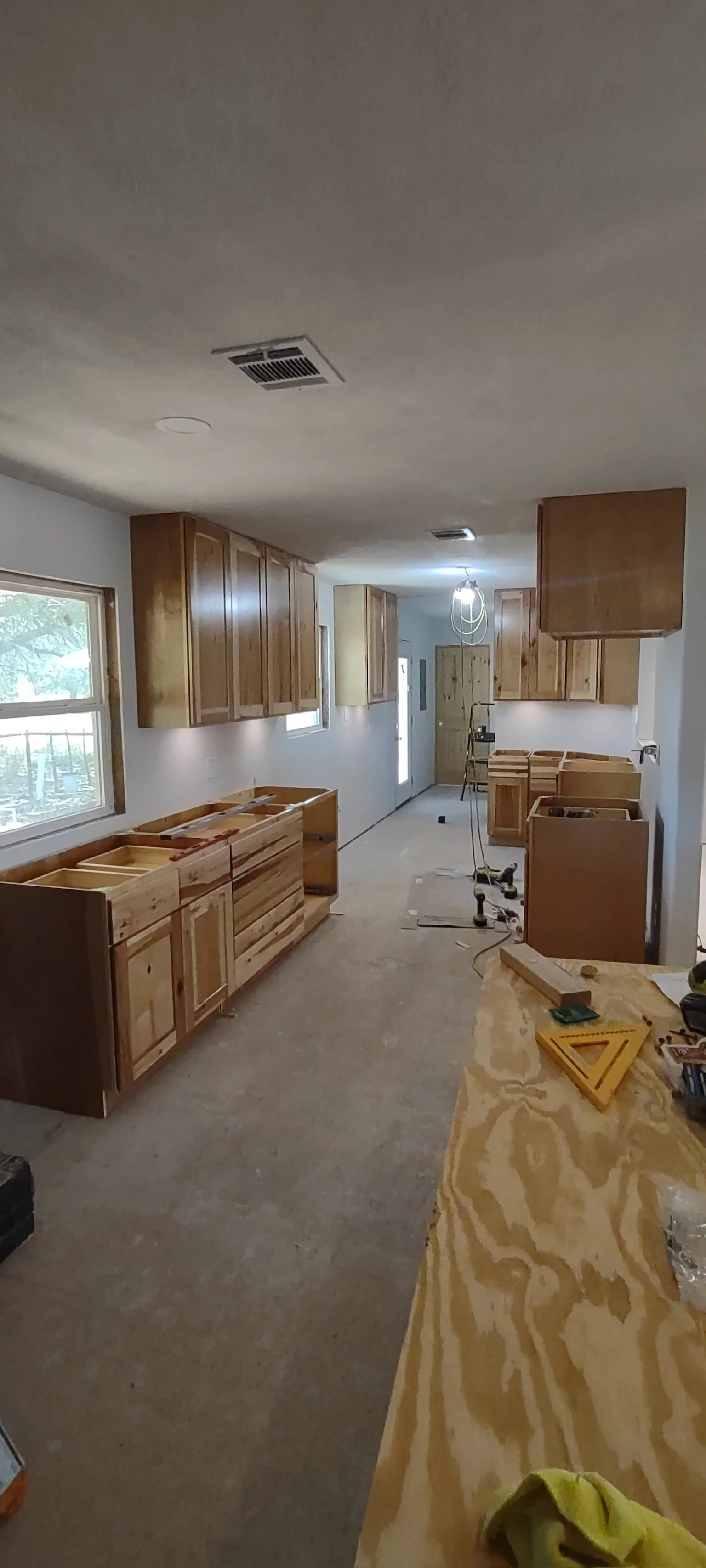 Kitchen under renovation with unfinished wooden cabinets, tools, and construction materials scattered around.