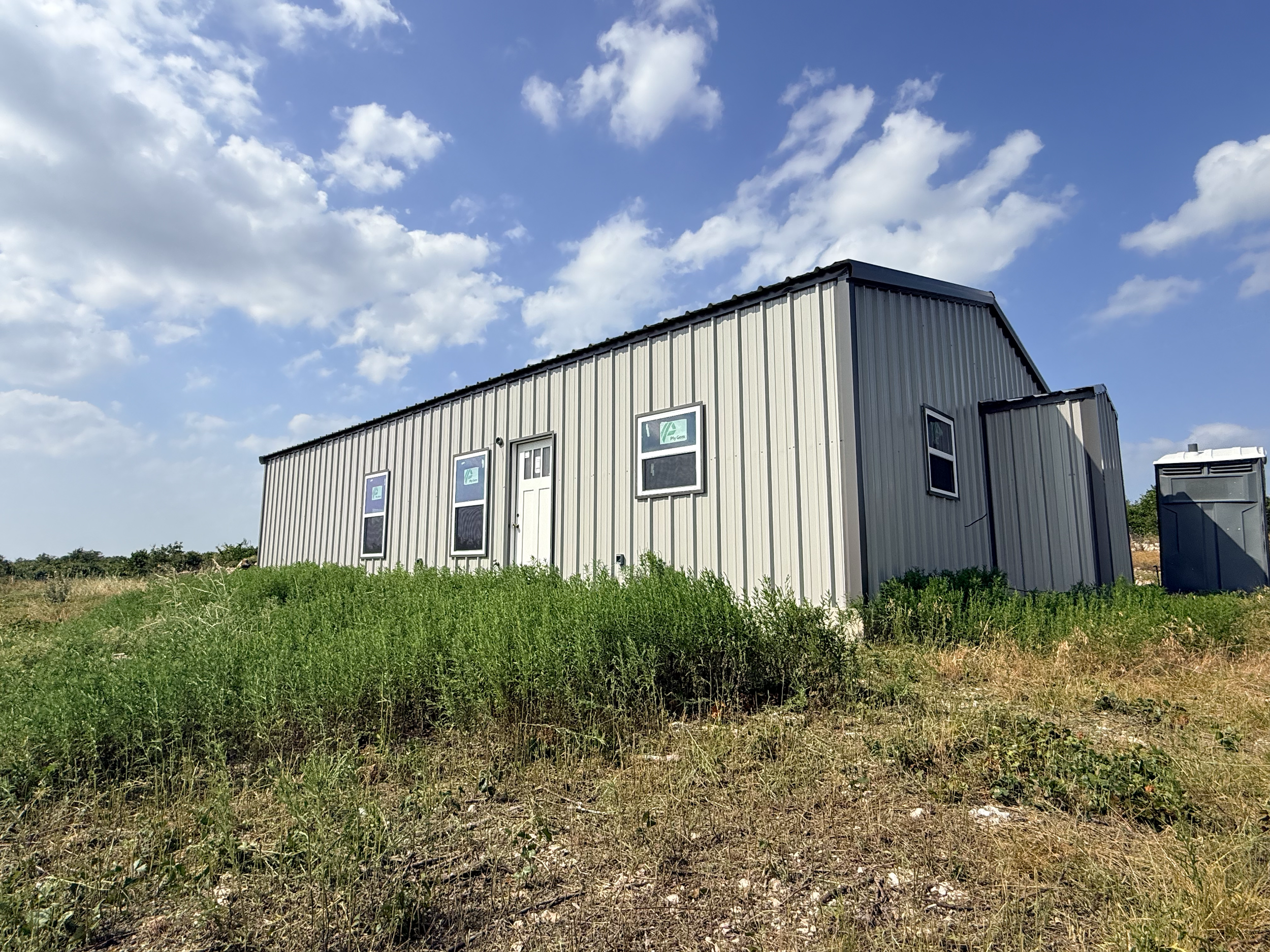 A metal building with rectangular windows situated on a grassy area under a partly cloudy sky.