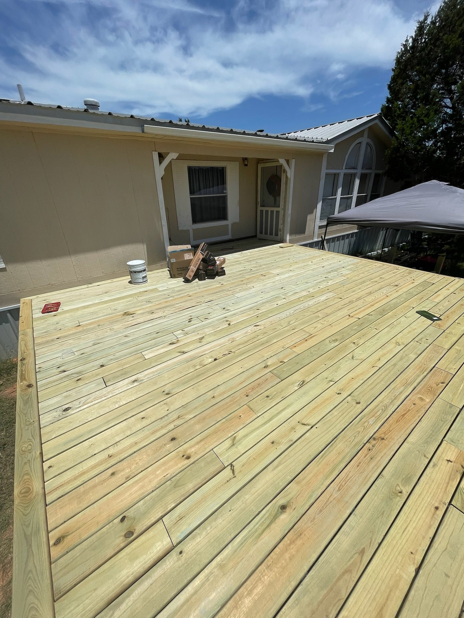 A new wooden deck being built outside a house with construction tools and materials on it, under a partly cloudy sky.