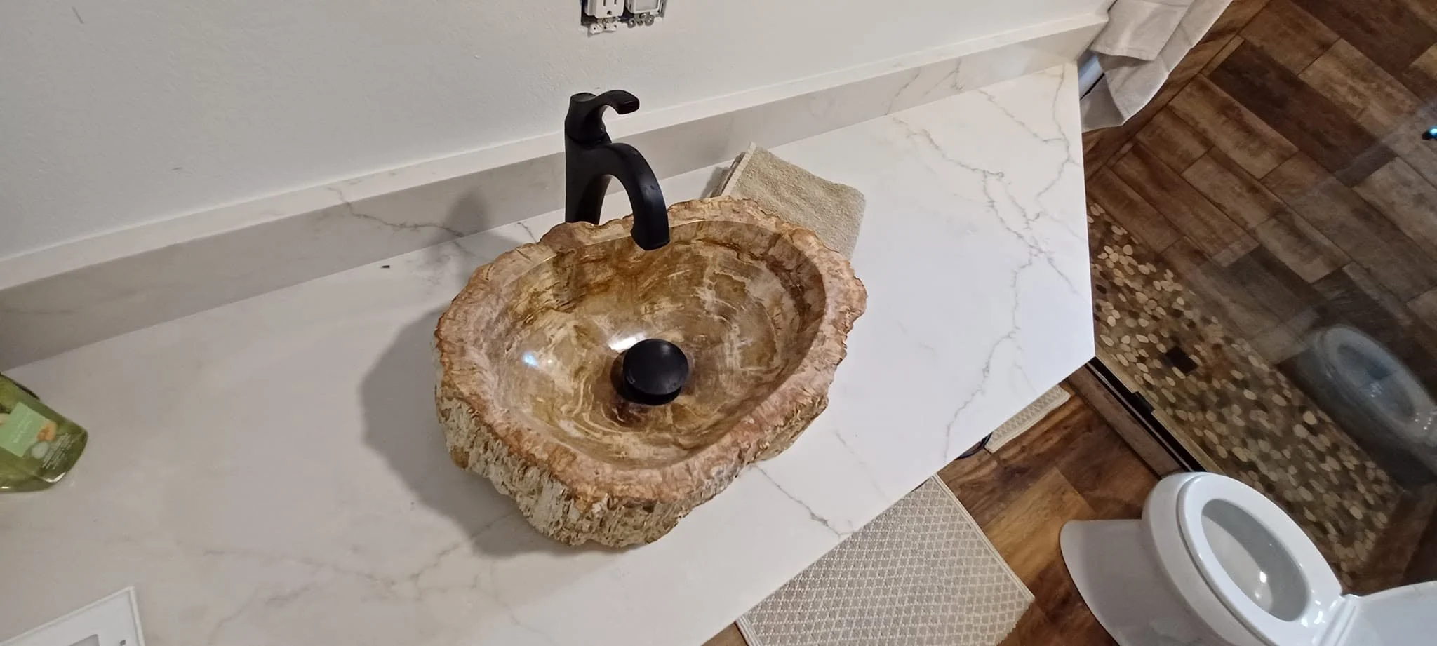 Bathroom with a natural stone sink, black faucet, white marble countertop, and wooden flooring.