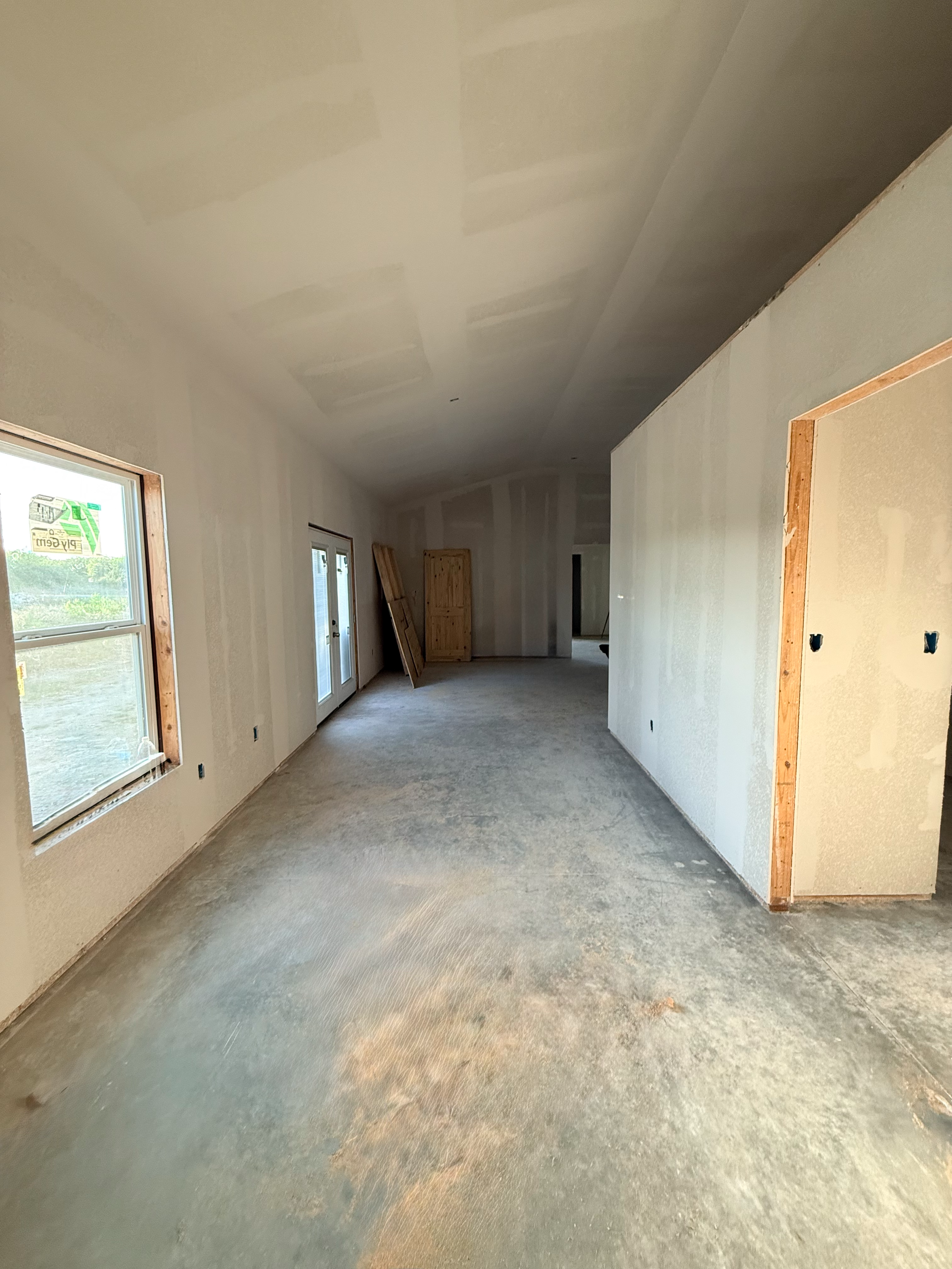 Interior view of a room under construction with unfinished drywall, framed door opening, and a concrete floor.