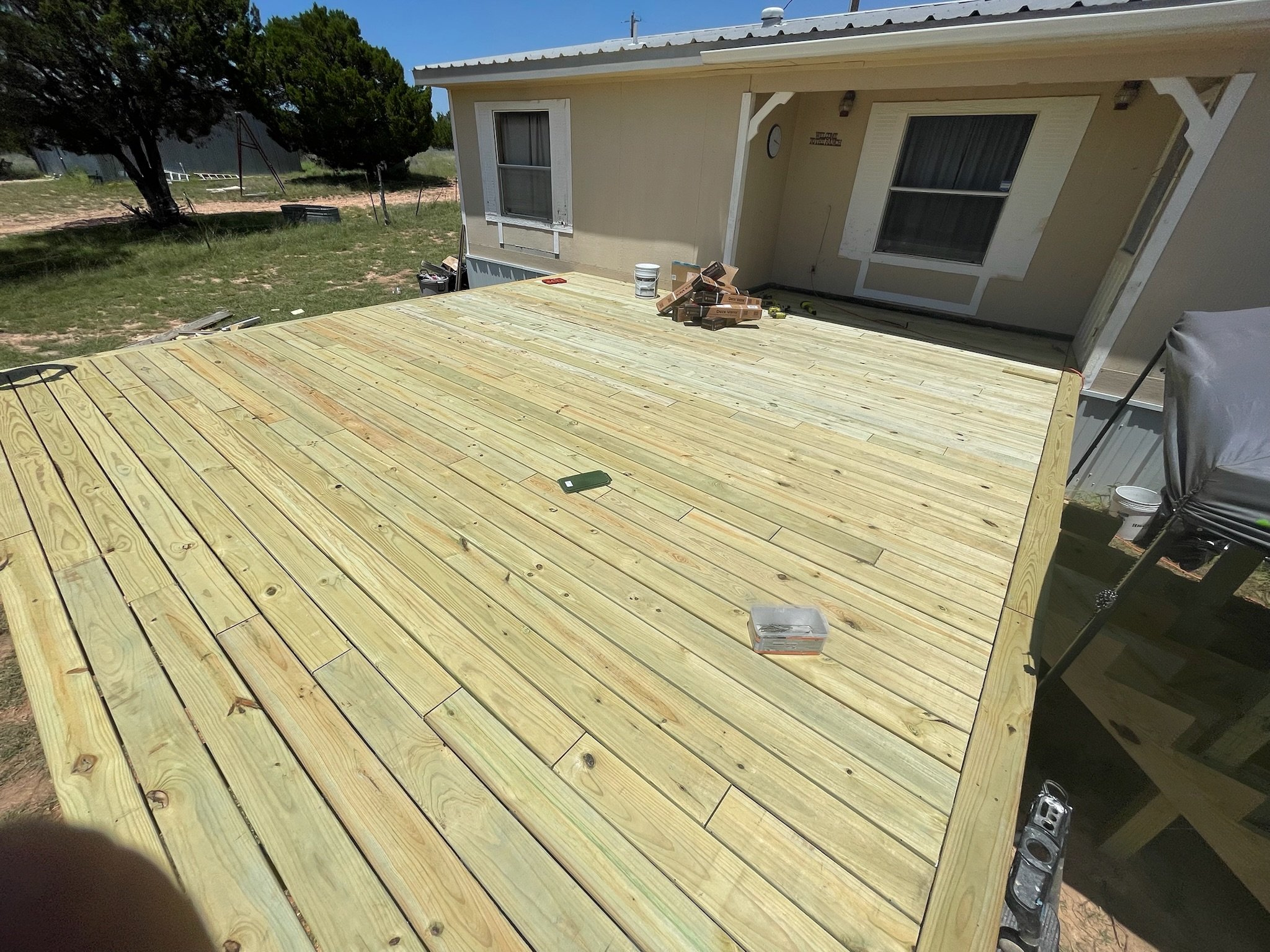 A partially built wooden deck outside a house with tools and materials on it, under a clear blue sky.