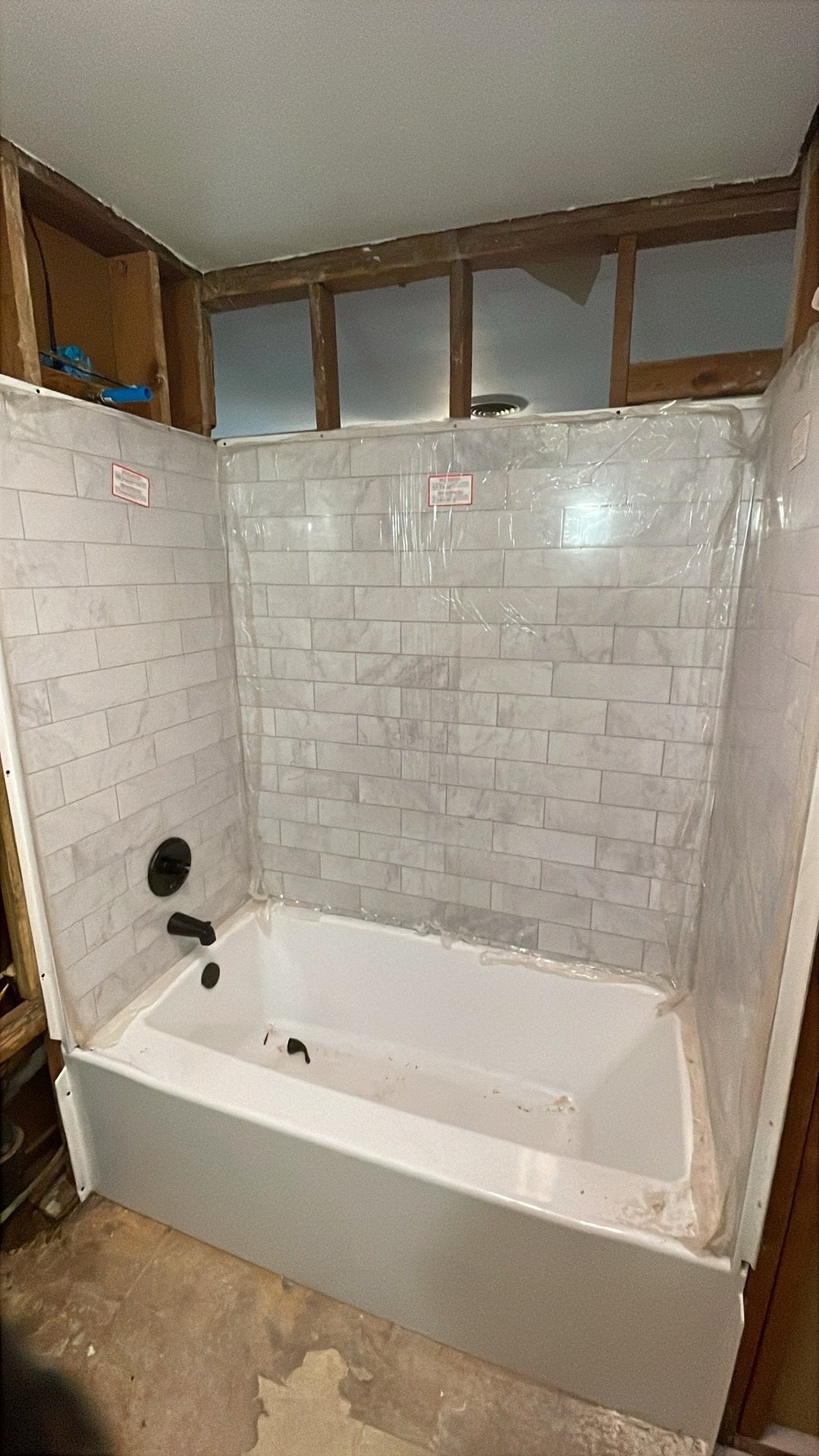 Bathroom with partially finished shower area, white bathtub, white tiled walls, and exposed wooden framing and ceiling.