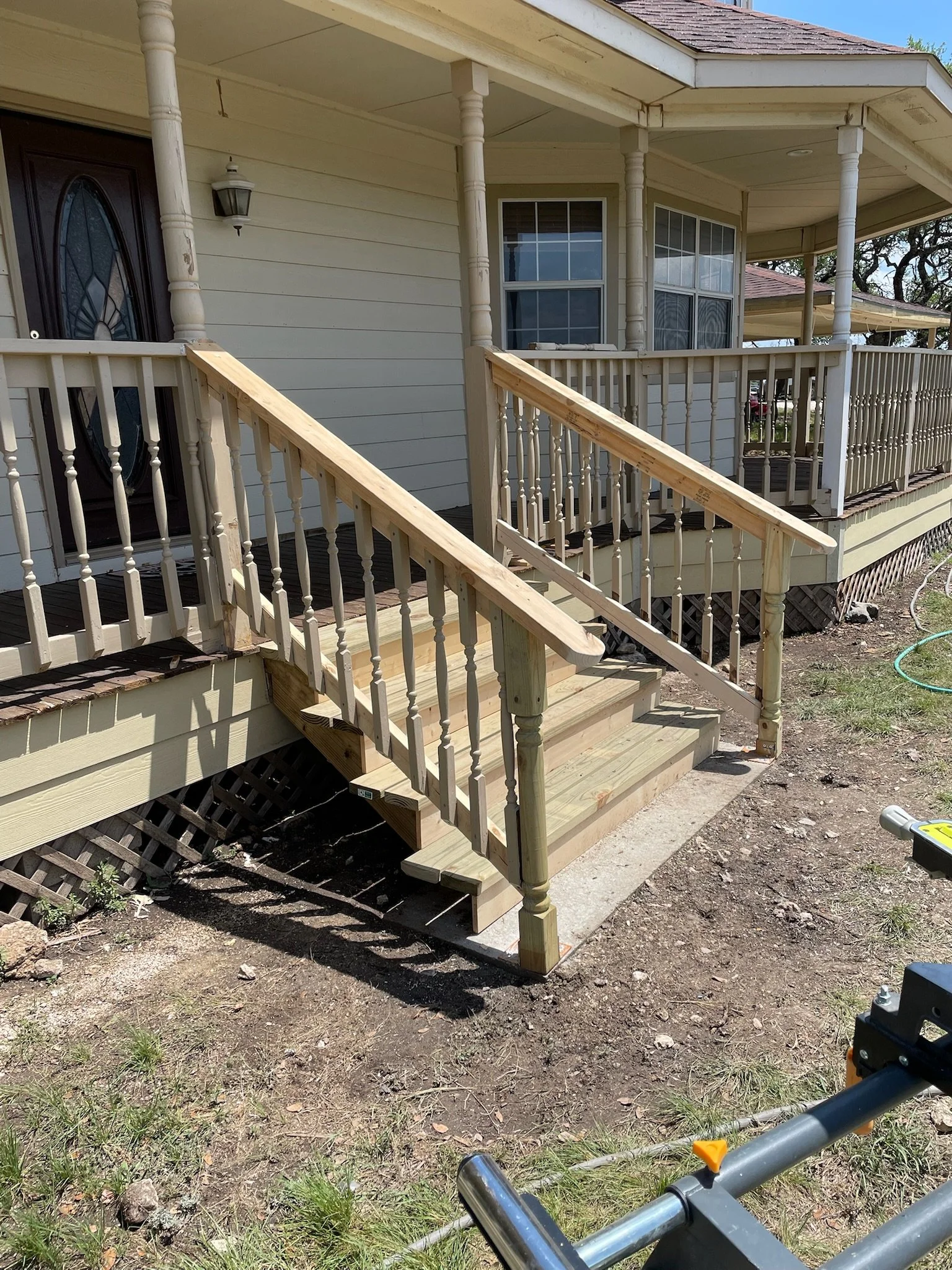A house with a front porch and a set of new wooden stairs leading up to the door, with tools and construction materials around.